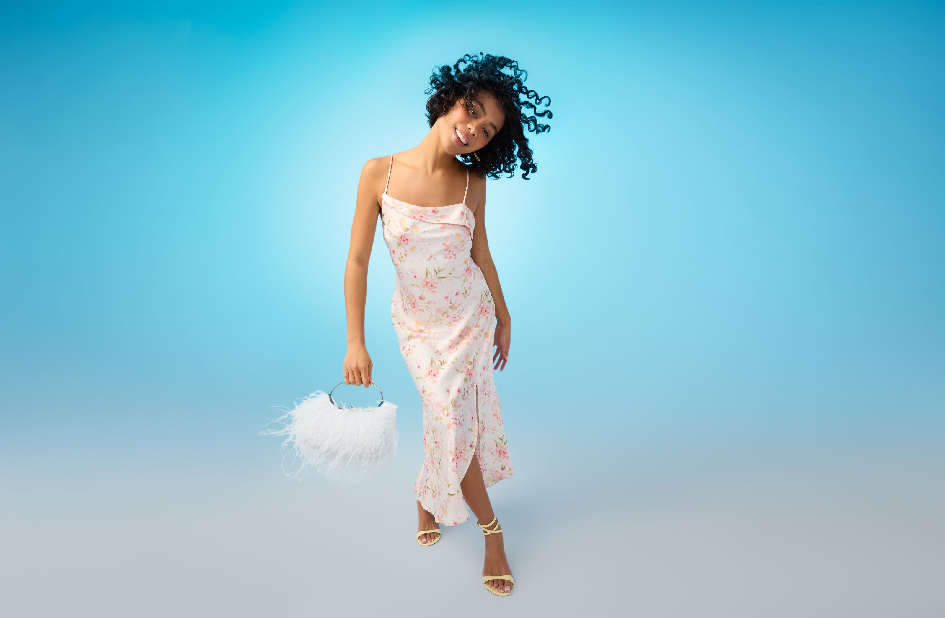 A woman wearing a slipdress and carrying a feathered handbag.