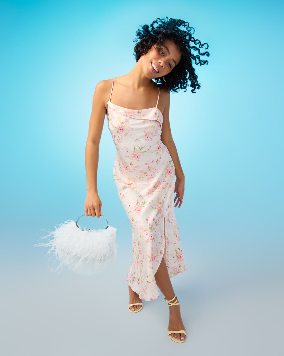 A woman wearing a slipdress and carrying a feathered handbag.