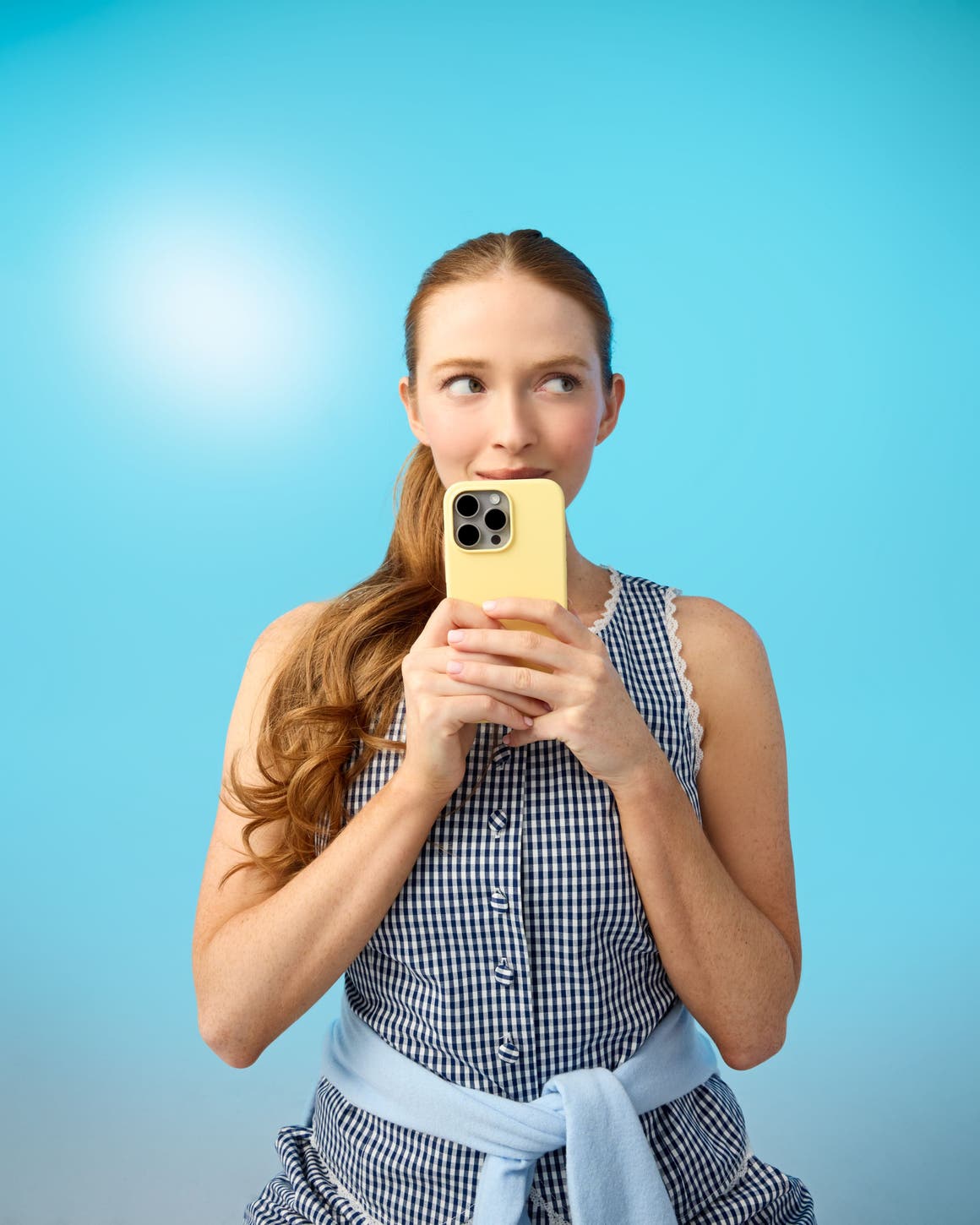 A woman wearing a green sweater and jeans and holding a phone.