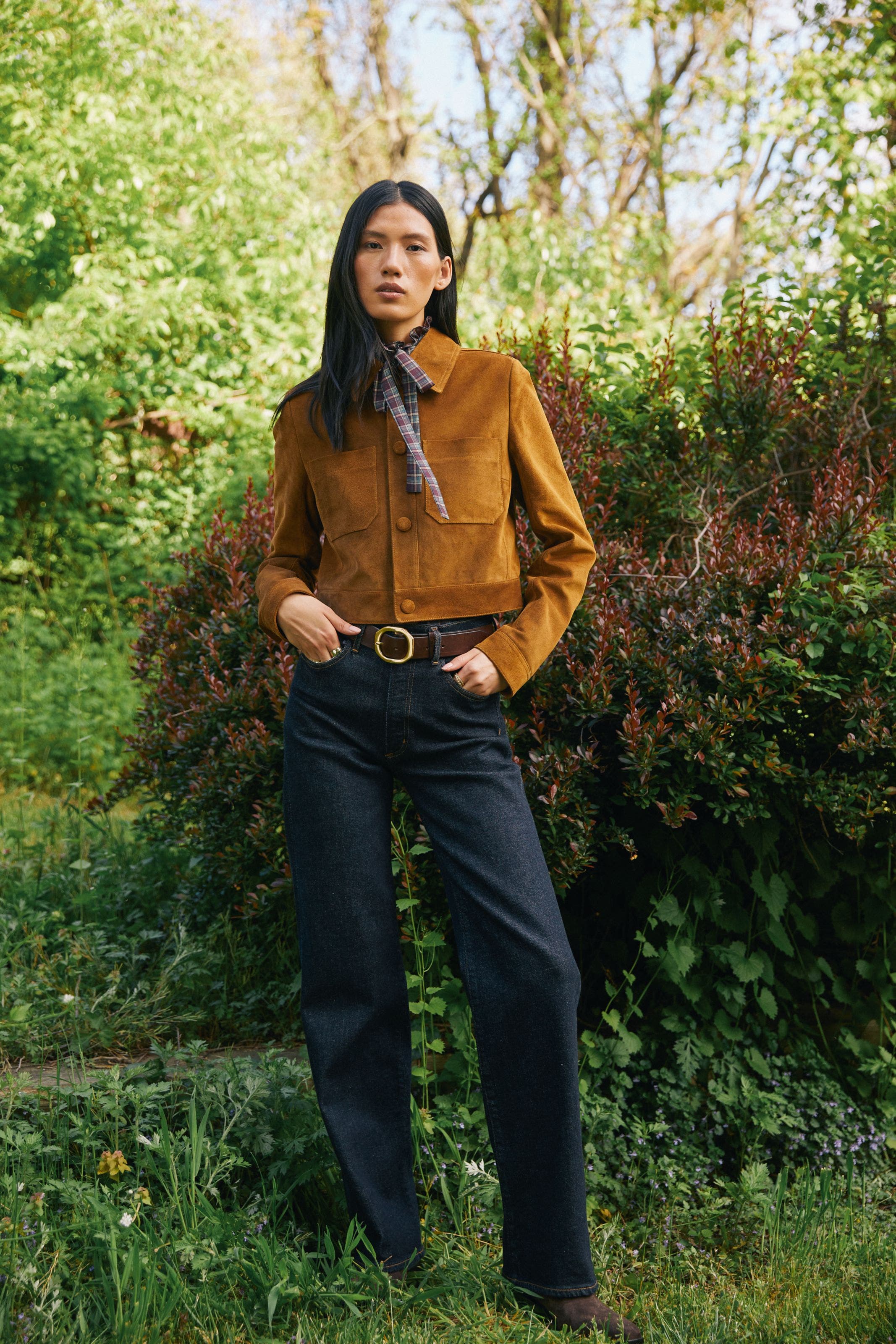 A woman wearing a cropped brown suede jacket and a pair of dark wash jeans.