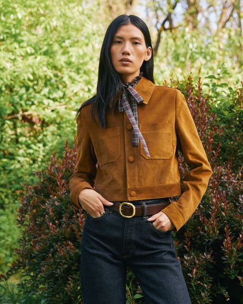A woman wearing a cropped brown suede jacket and a pair of dark wash jeans.