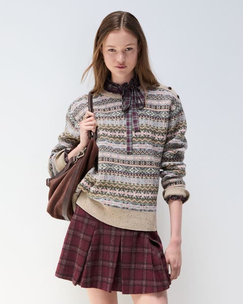 A woman wearing a fair isle sweater and a pleated plaid skirt.