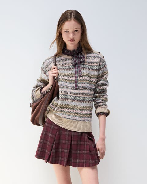 A woman wearing a Fair Isle sweater over a plaid dress.