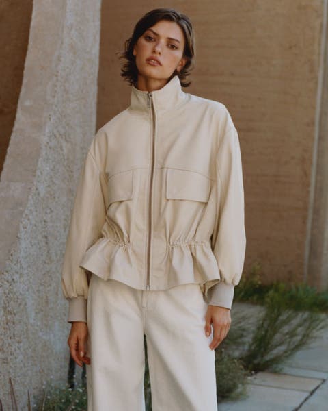 A woman wearing an off-white cinched-waist jacket.