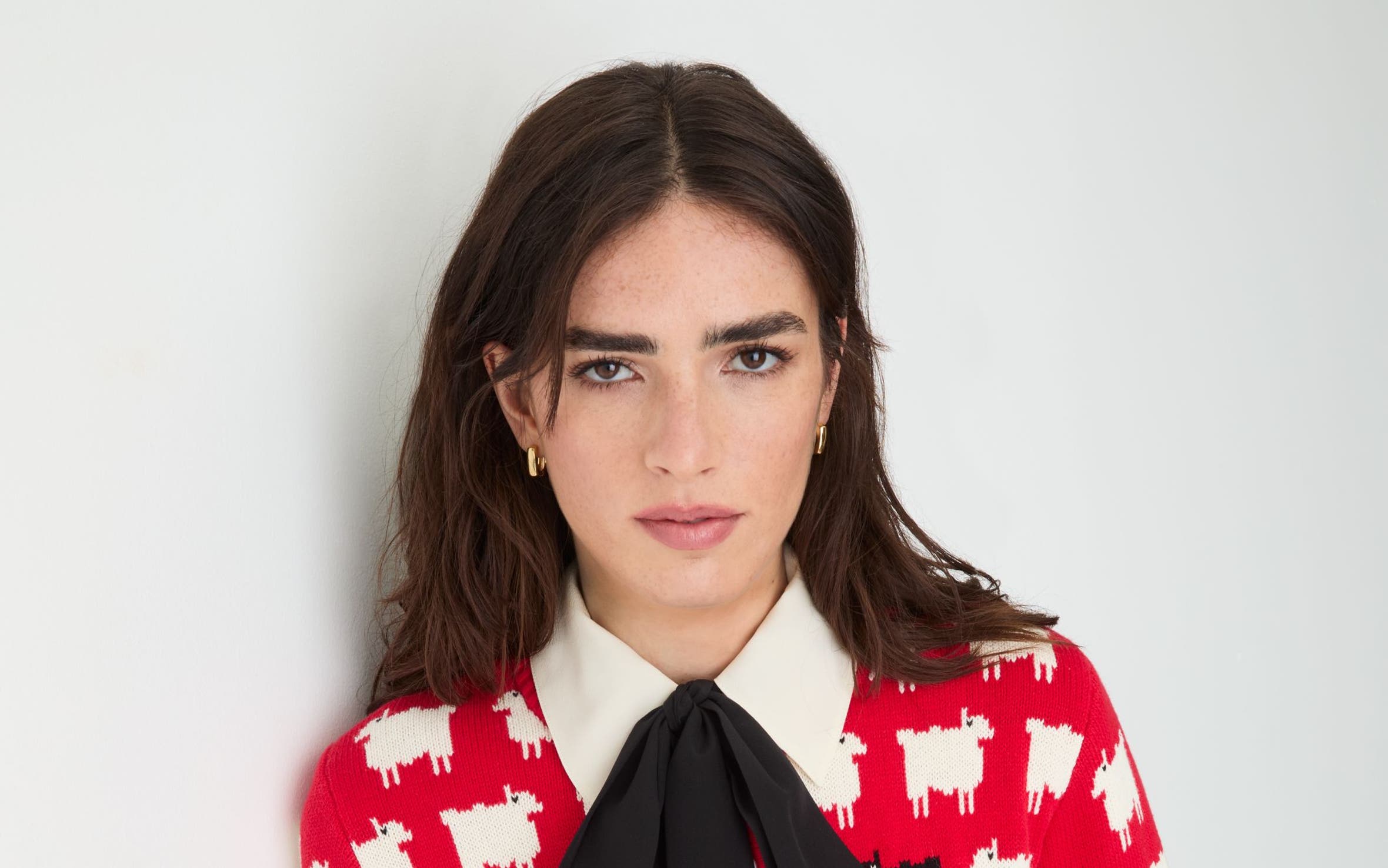 A woman wearing a bright red knit sweater patterned with small white sheep and one black sheep.