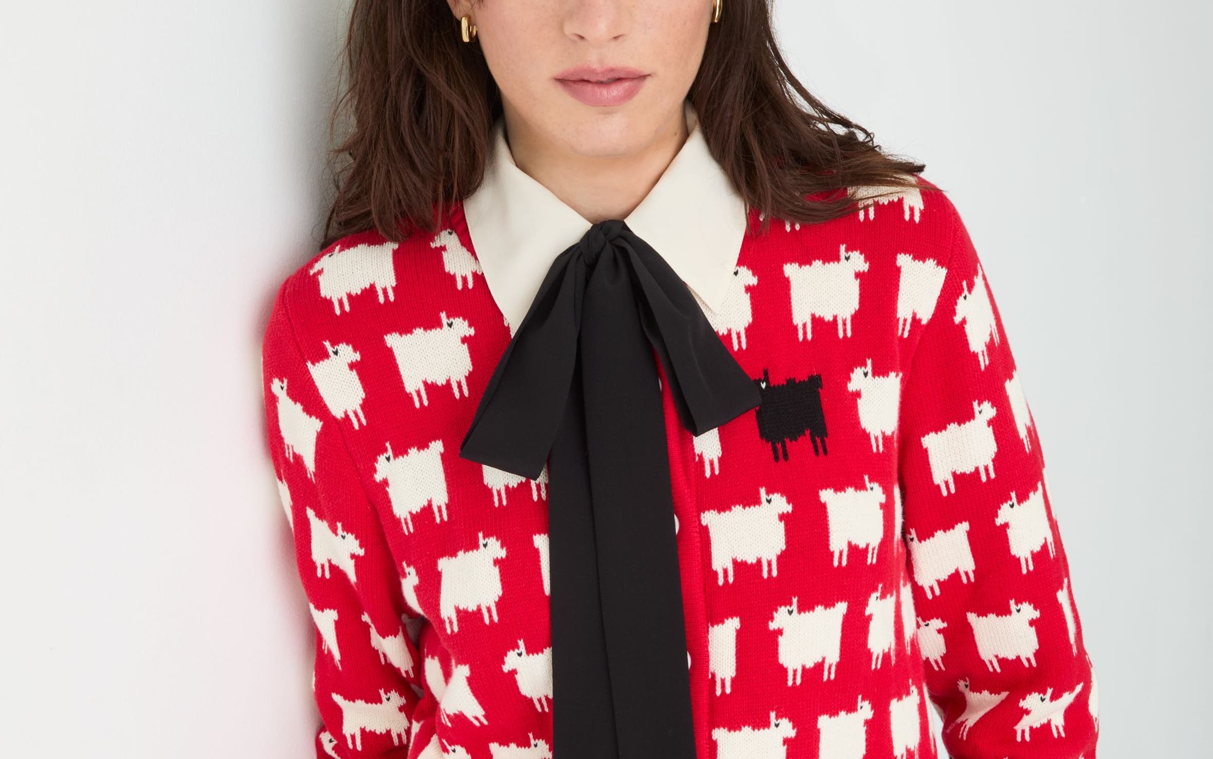 A woman wearing a bright red knit sweater patterned with small white sheep and one black sheep.