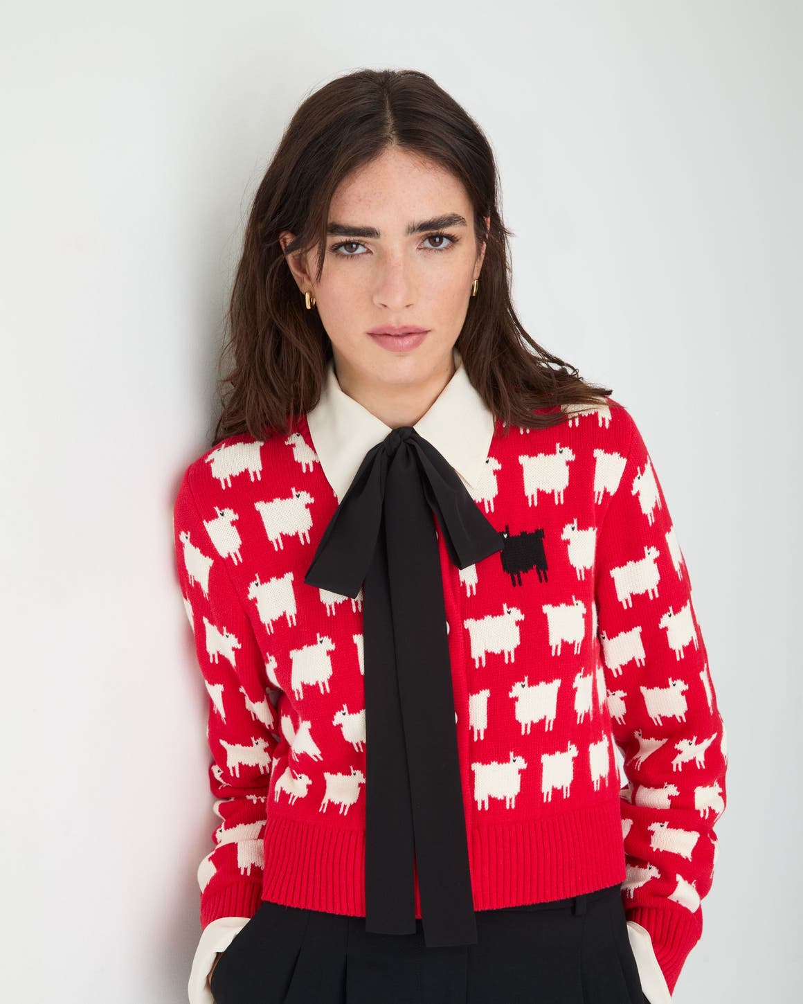A woman wearing a bright red knit sweater patterned with small white sheep and one black sheep.