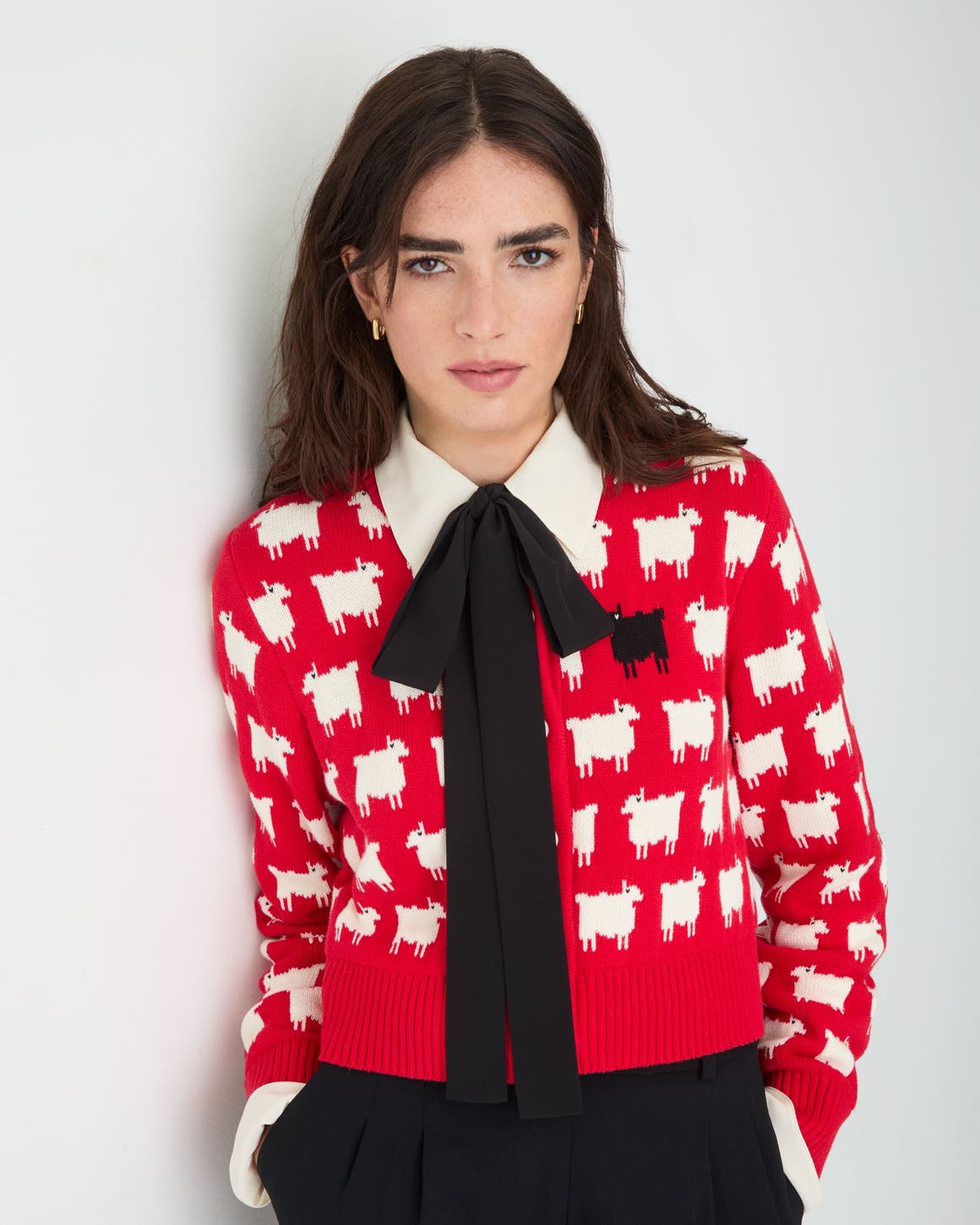 A woman wearing a bright red knit sweater patterned with small white sheep and one black sheep.