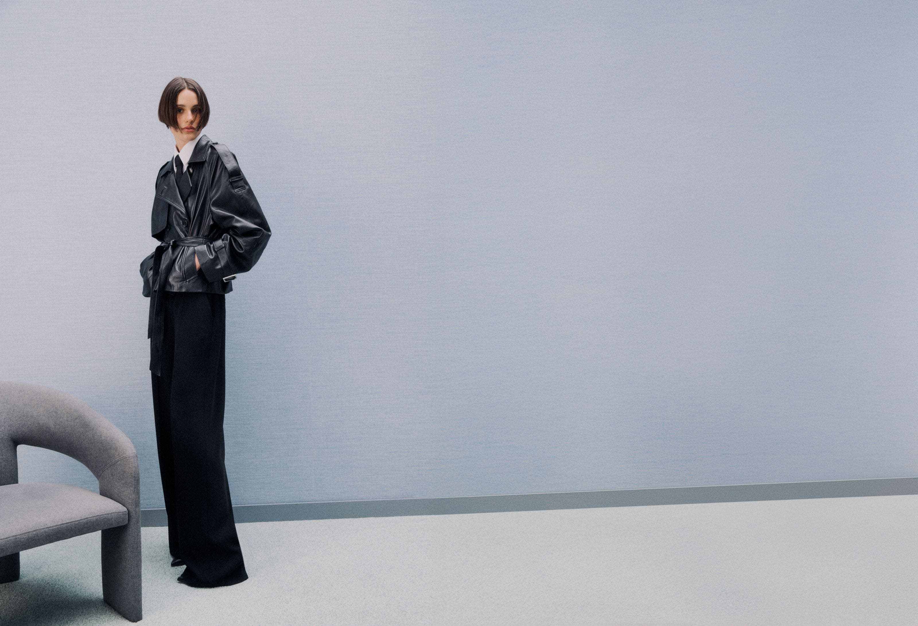 Woman wearing a black leather jacket, white button-down shirt, black tie, black work pants and heels.