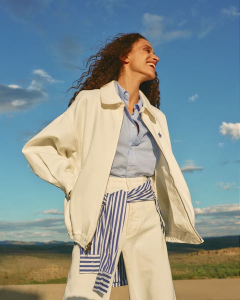 Woman wearing a matching jacket and pants with a blue shirt and a striped shirt tied around the waist.