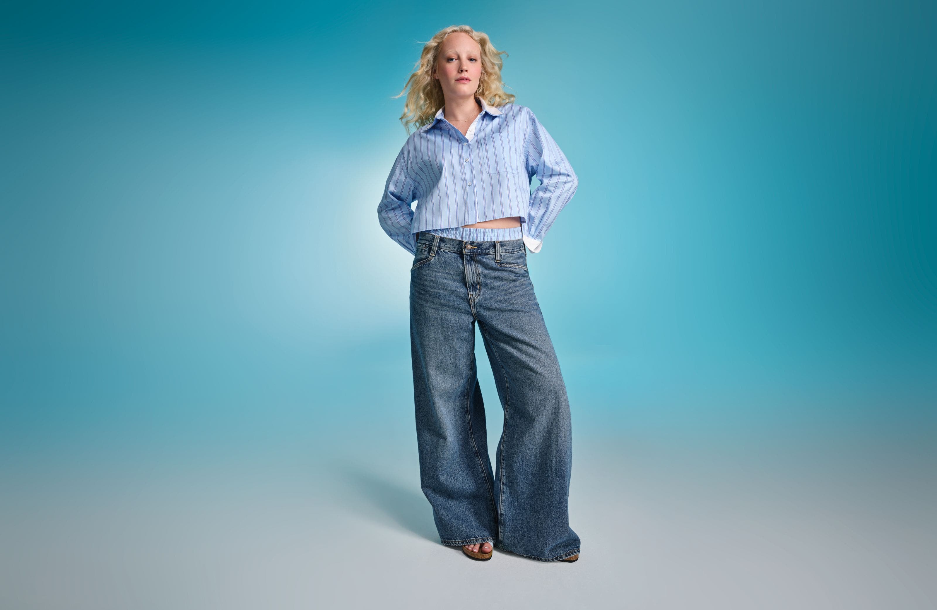 A woman wearing a striped blue shirt with wide-leg blue jeans.