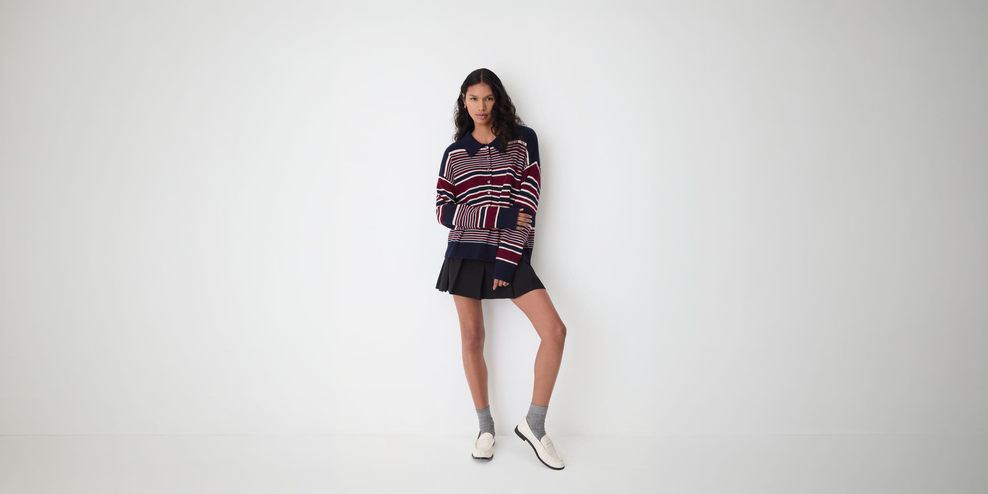 A woman in a striped cardigan and pleated skirt.