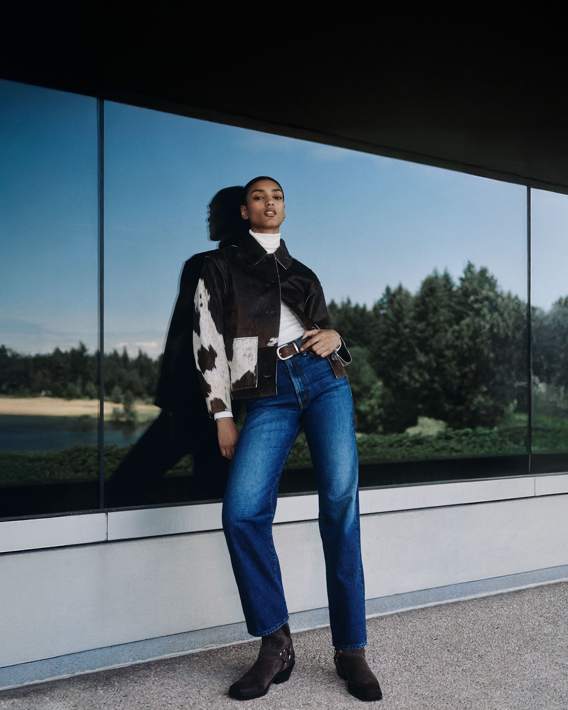 Woman wearing an animal-print jacket, white turtleneck, denim jeans and boots.