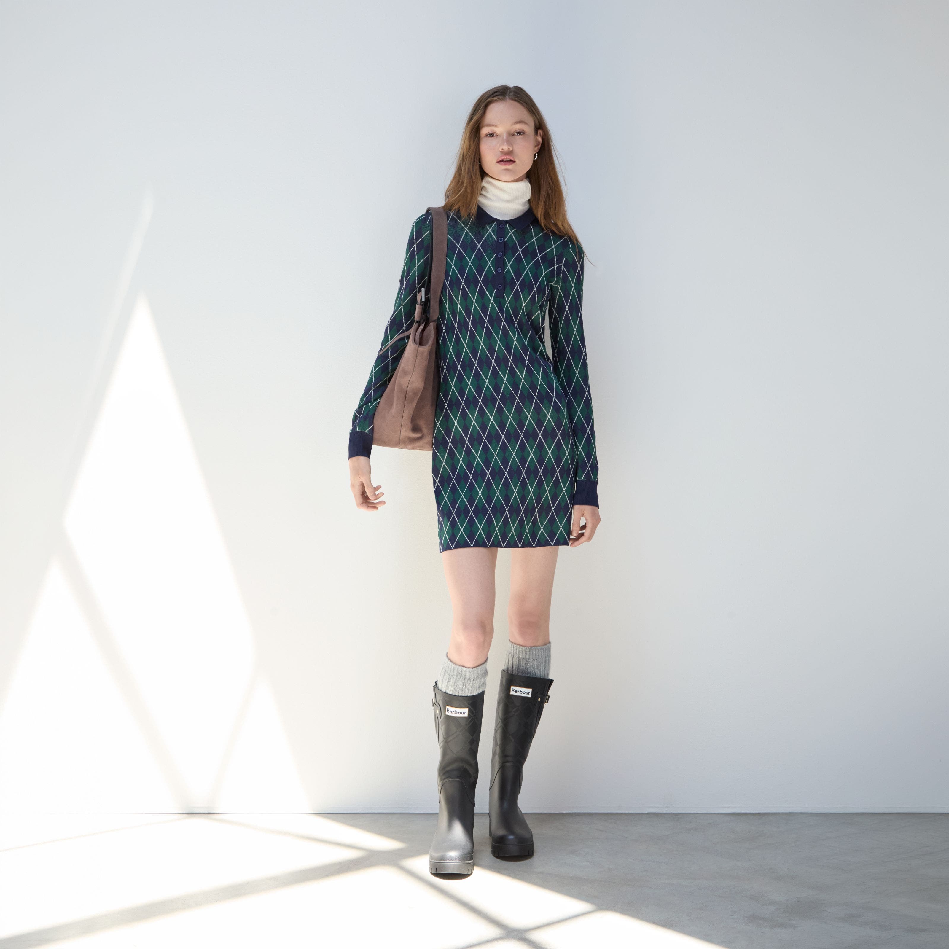 A woman wearing an argyle sweater dress and Hunter boots.
