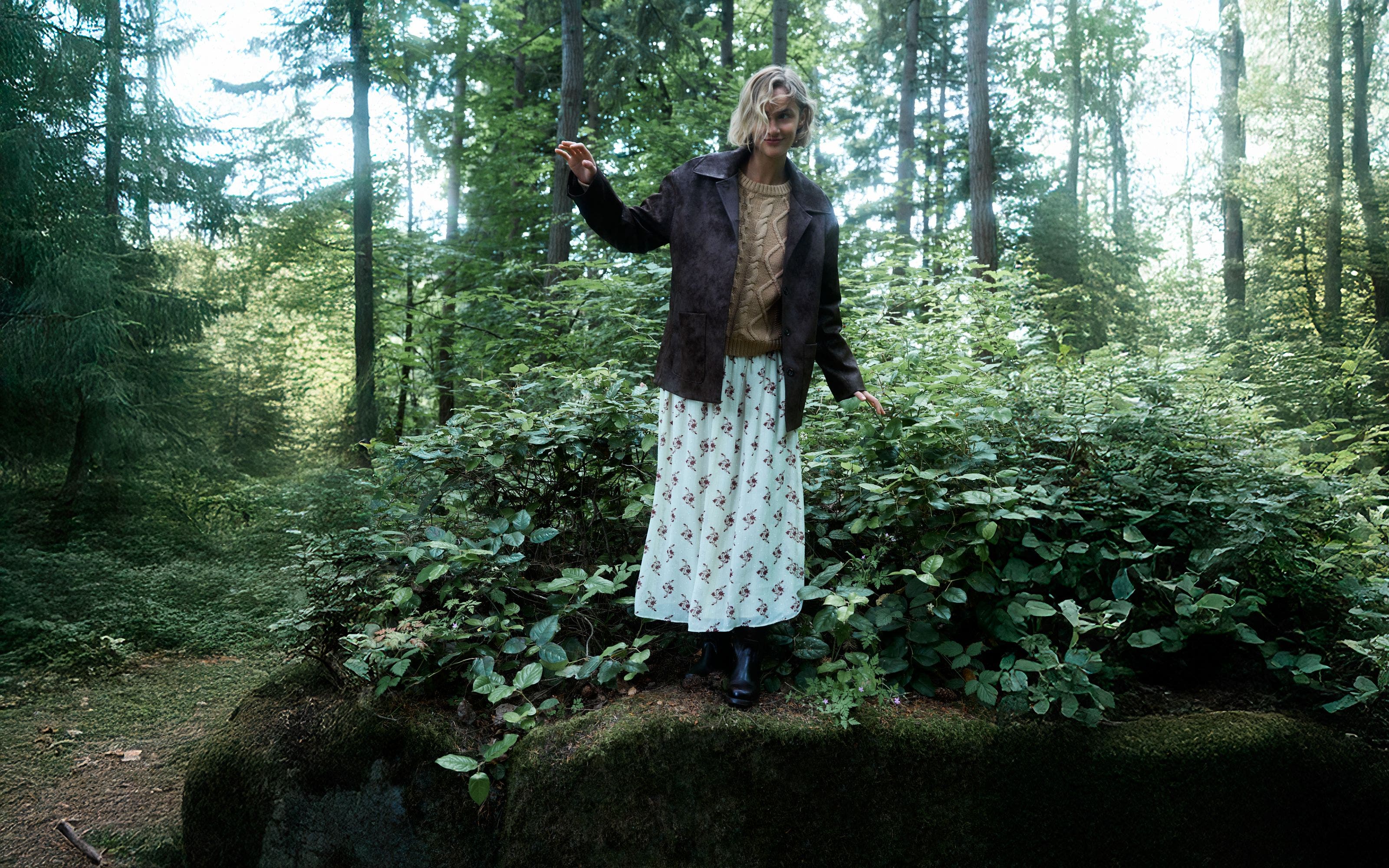 Woman wearing a suede jacket, sweater, printed skirt and boots.