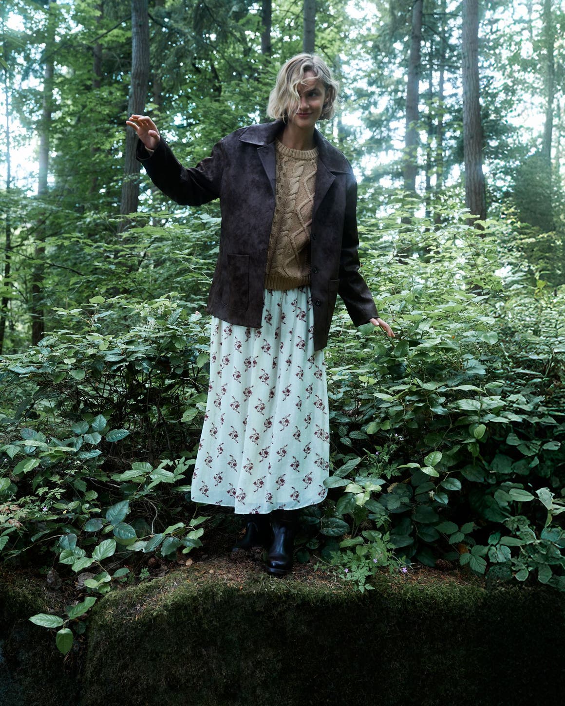 Woman wearing a suede jacket, sweater, printed skirt and boots.
