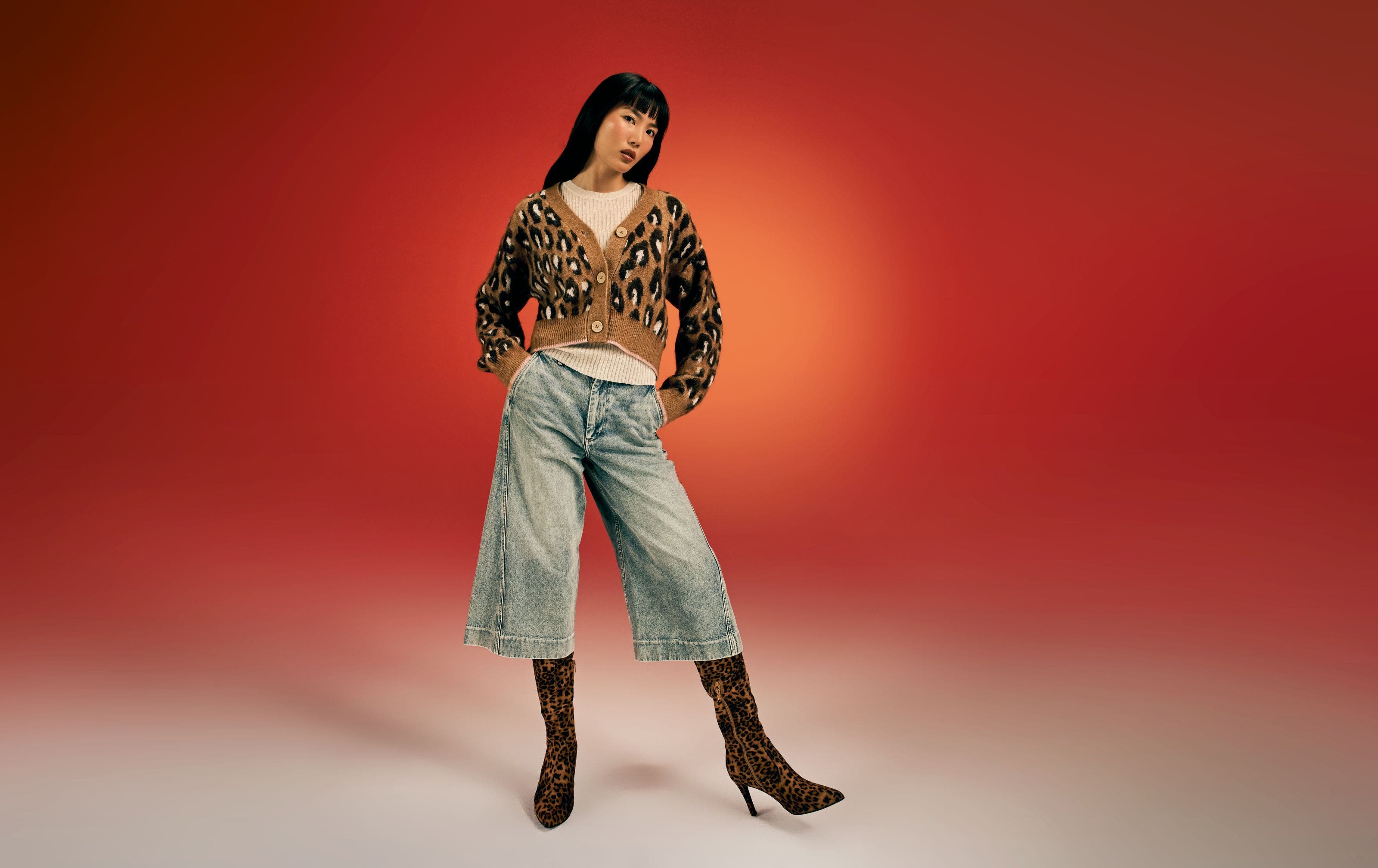 A woman wearing a leopard-print cardigan with jeans and boots. 