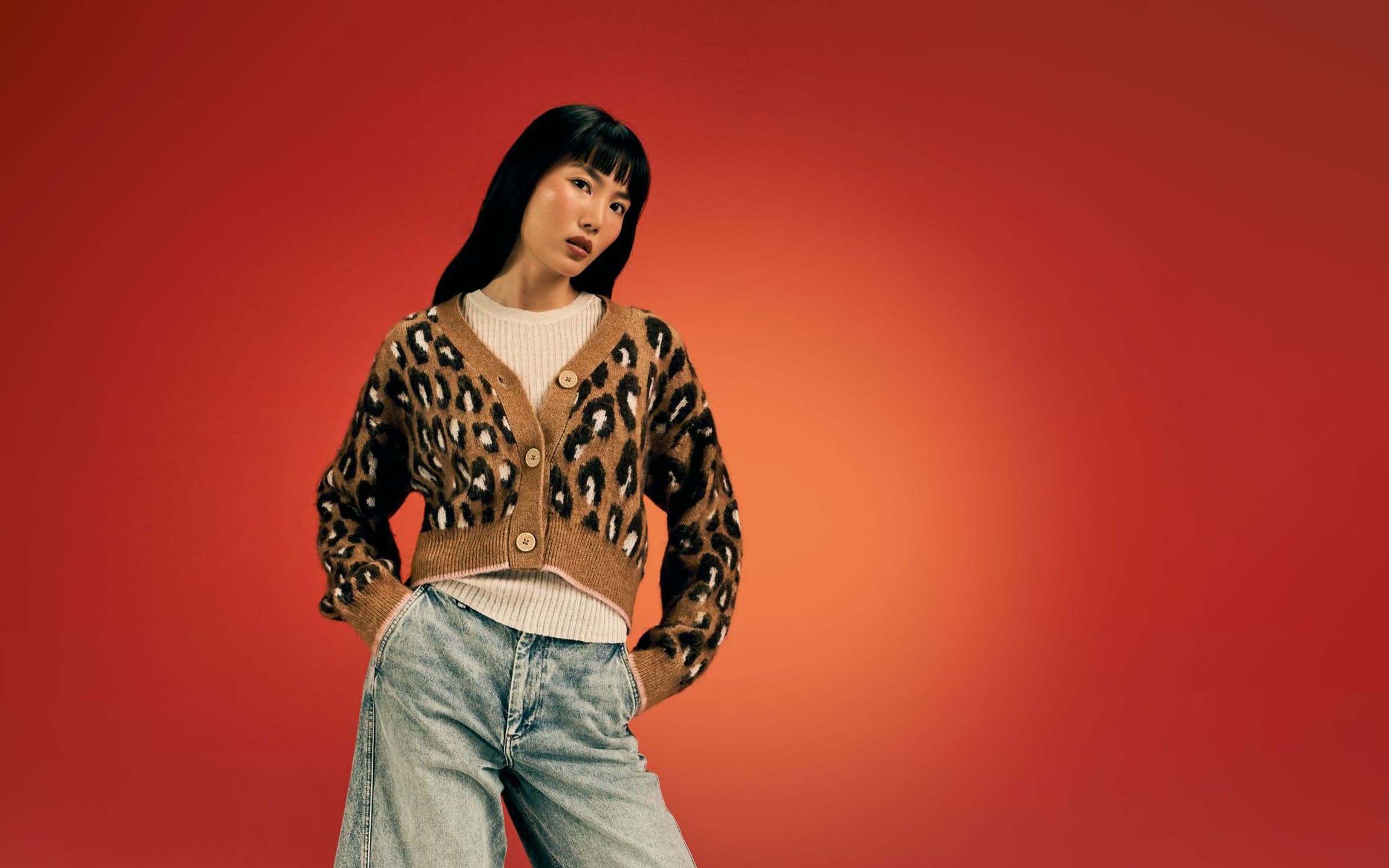 A woman wearing a leopard-print cardigan with jeans and boots.