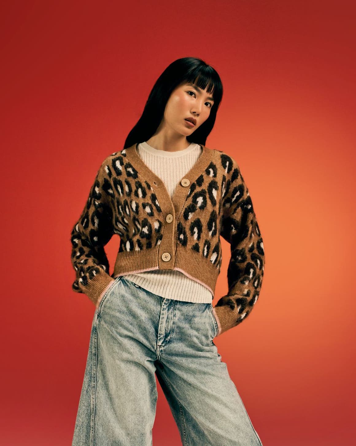 A woman wearing a leopard-print cardigan with jeans and boots.