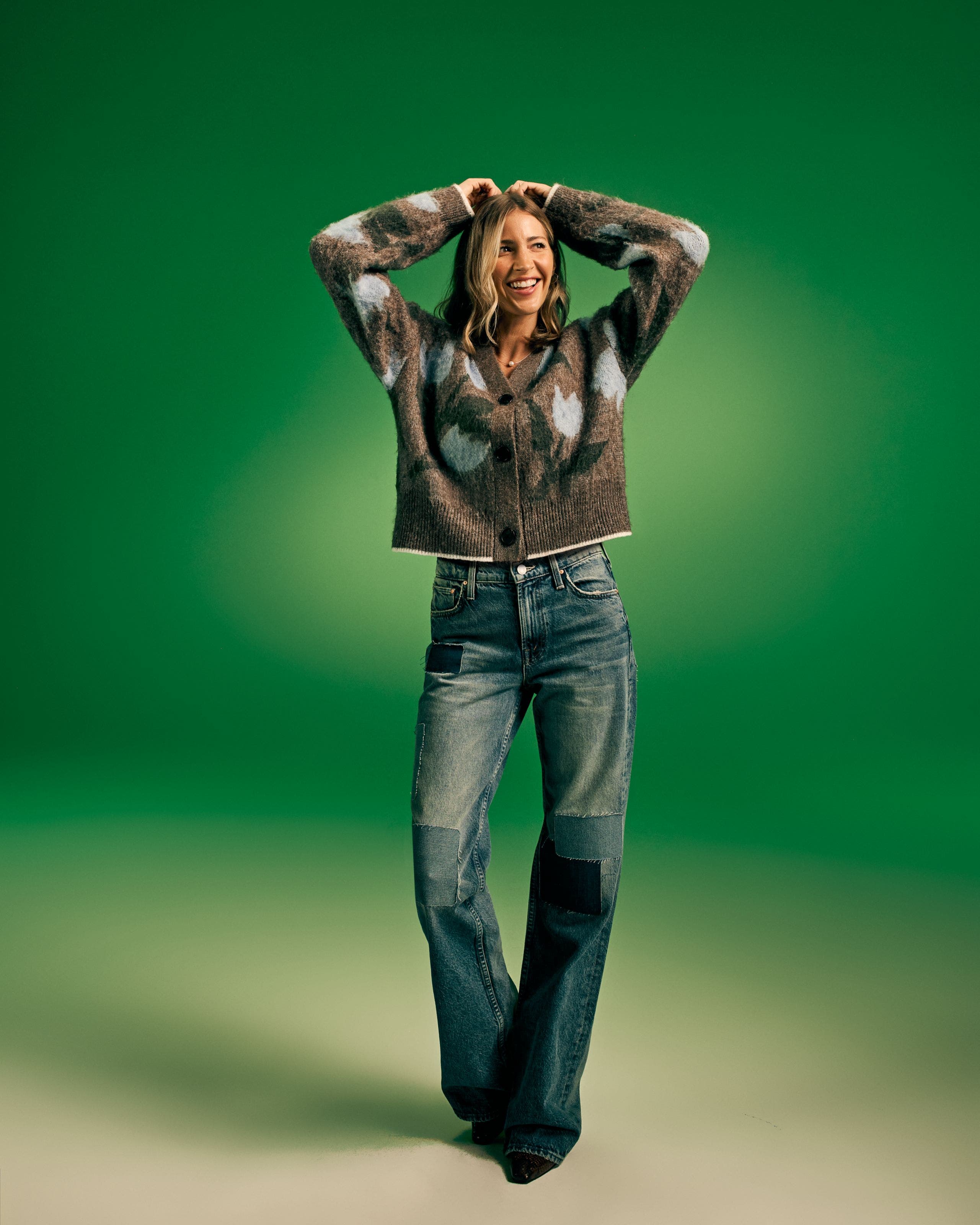 Woman in a knit cardigan and patchwork wide-leg jeans on green.