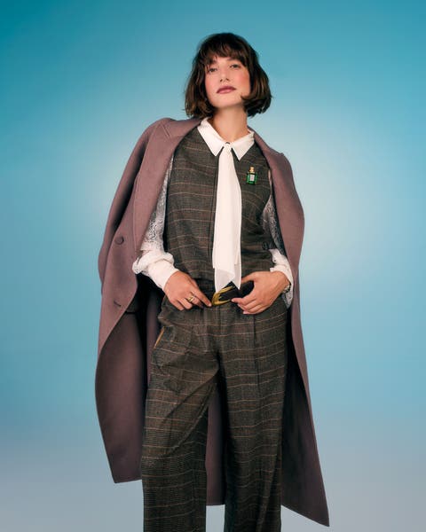 A woman wearing a plaid vest and trousers suit set with a white blouse and draped coat.