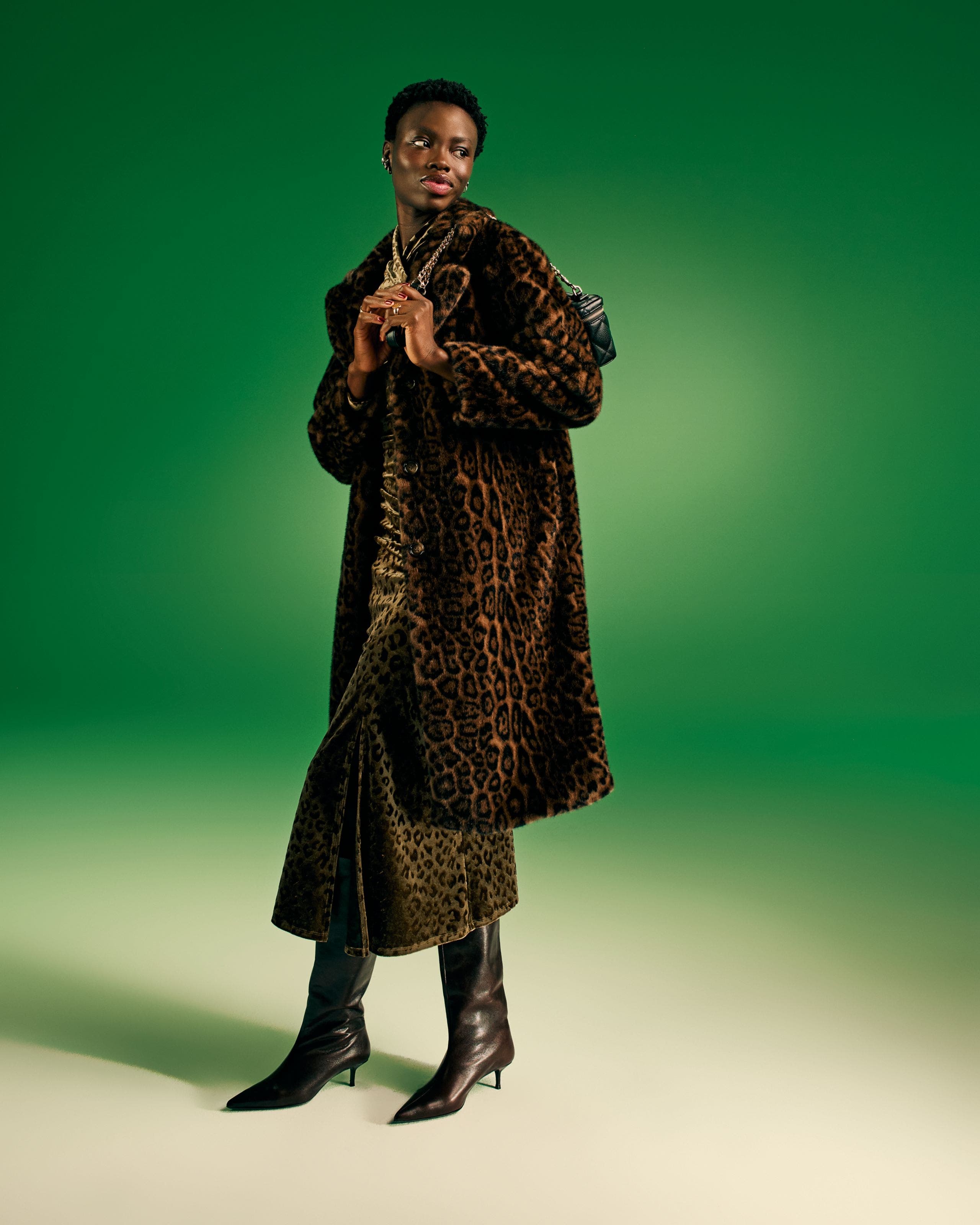 Woman in a long leopard-print coat and black boots on green.