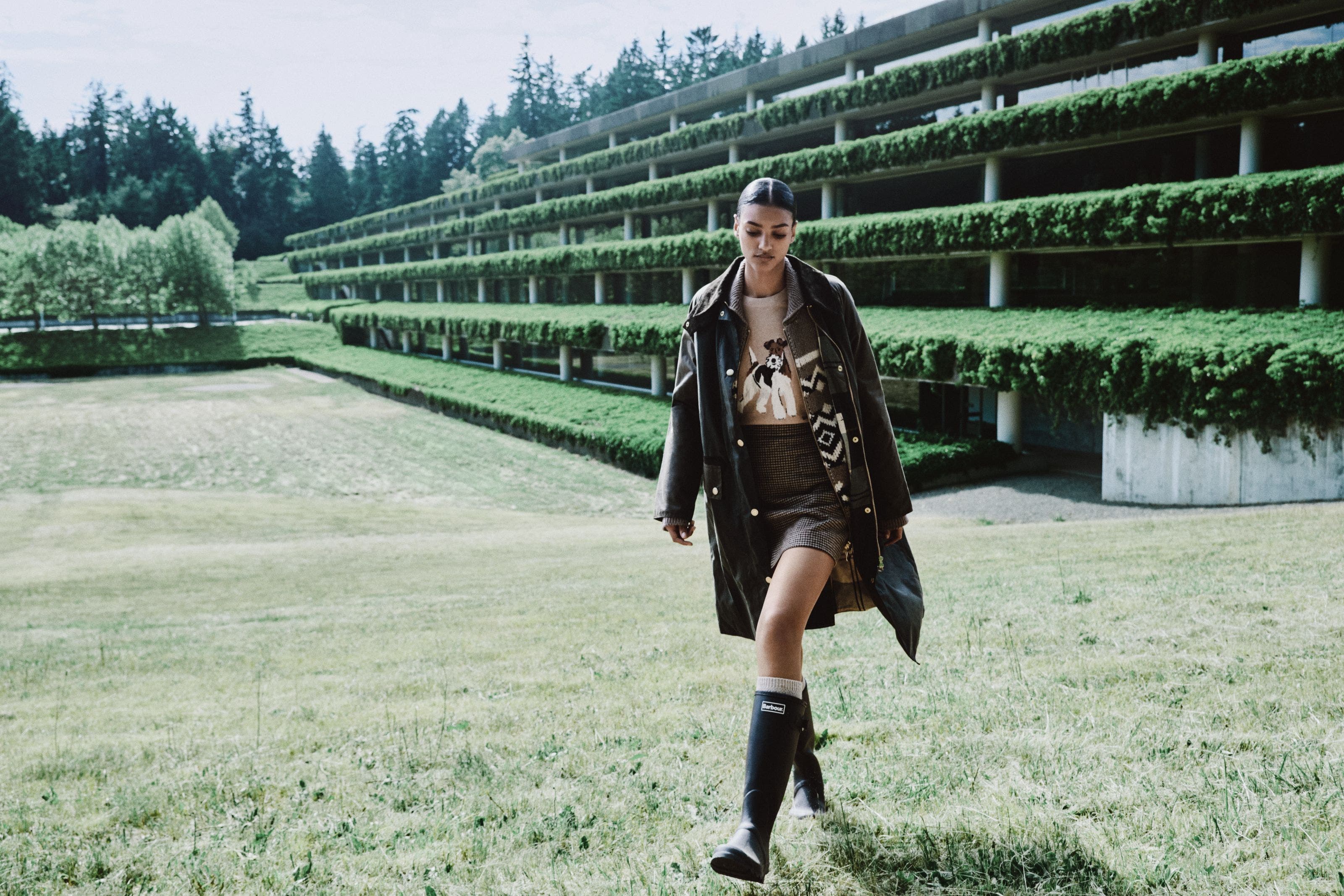 Woman wearing a parka, cardigan, tweed skirt and rain boots.