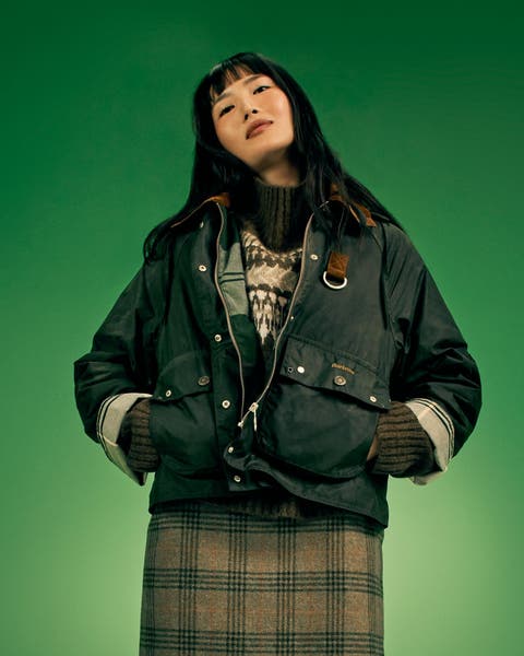 Woman in a waxed jacket, sweater, and plaid skirt.