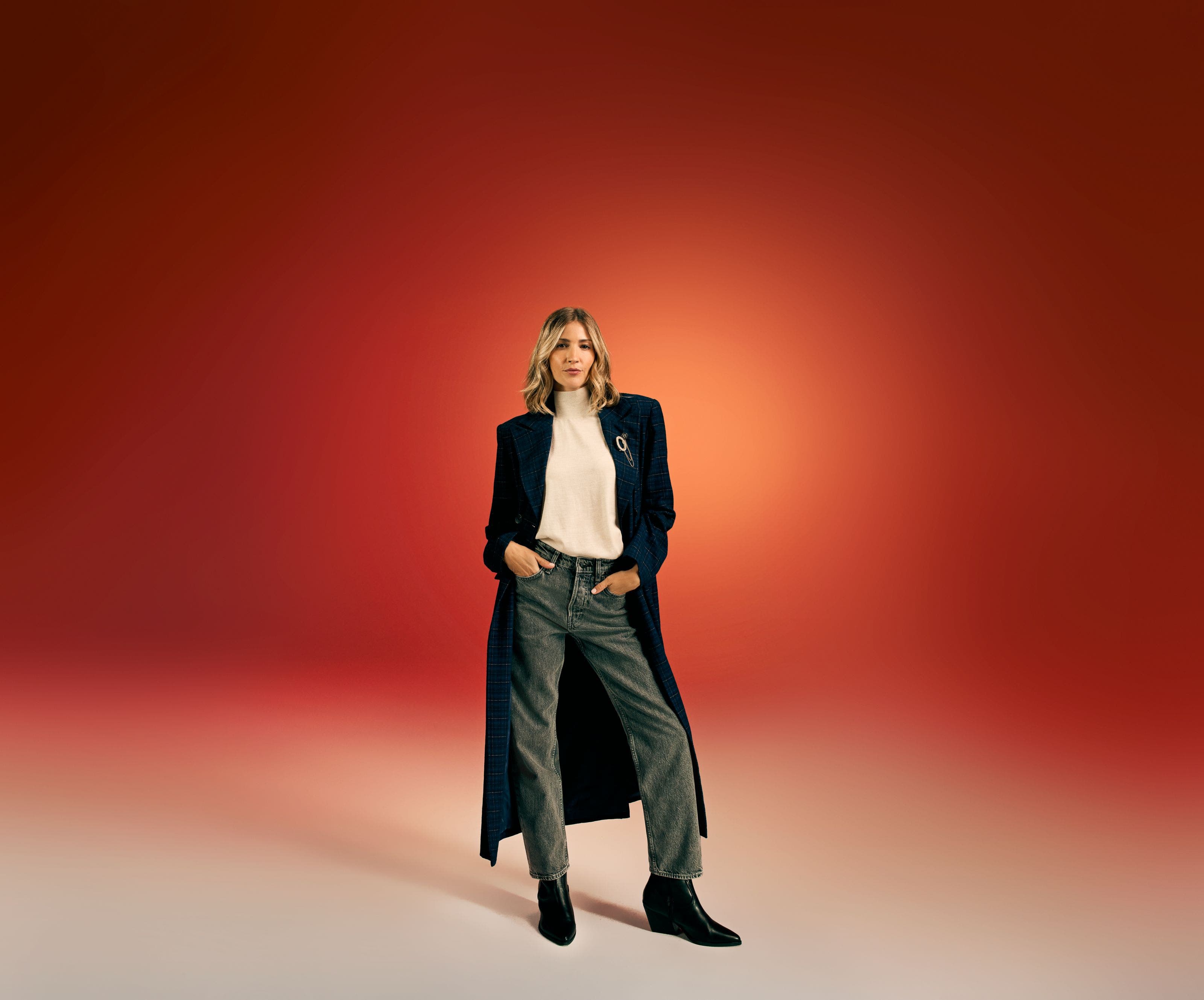 A woman wearing a black coat, white top and grey jeans.