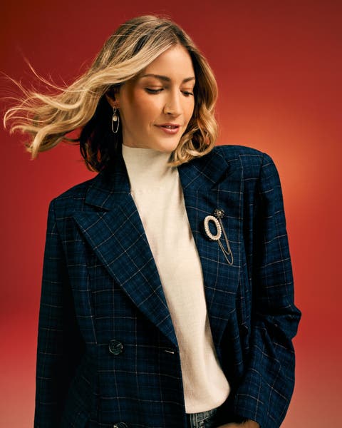 Woman in a navy plaid blazer with a pearl brooch and cream mock-neck.