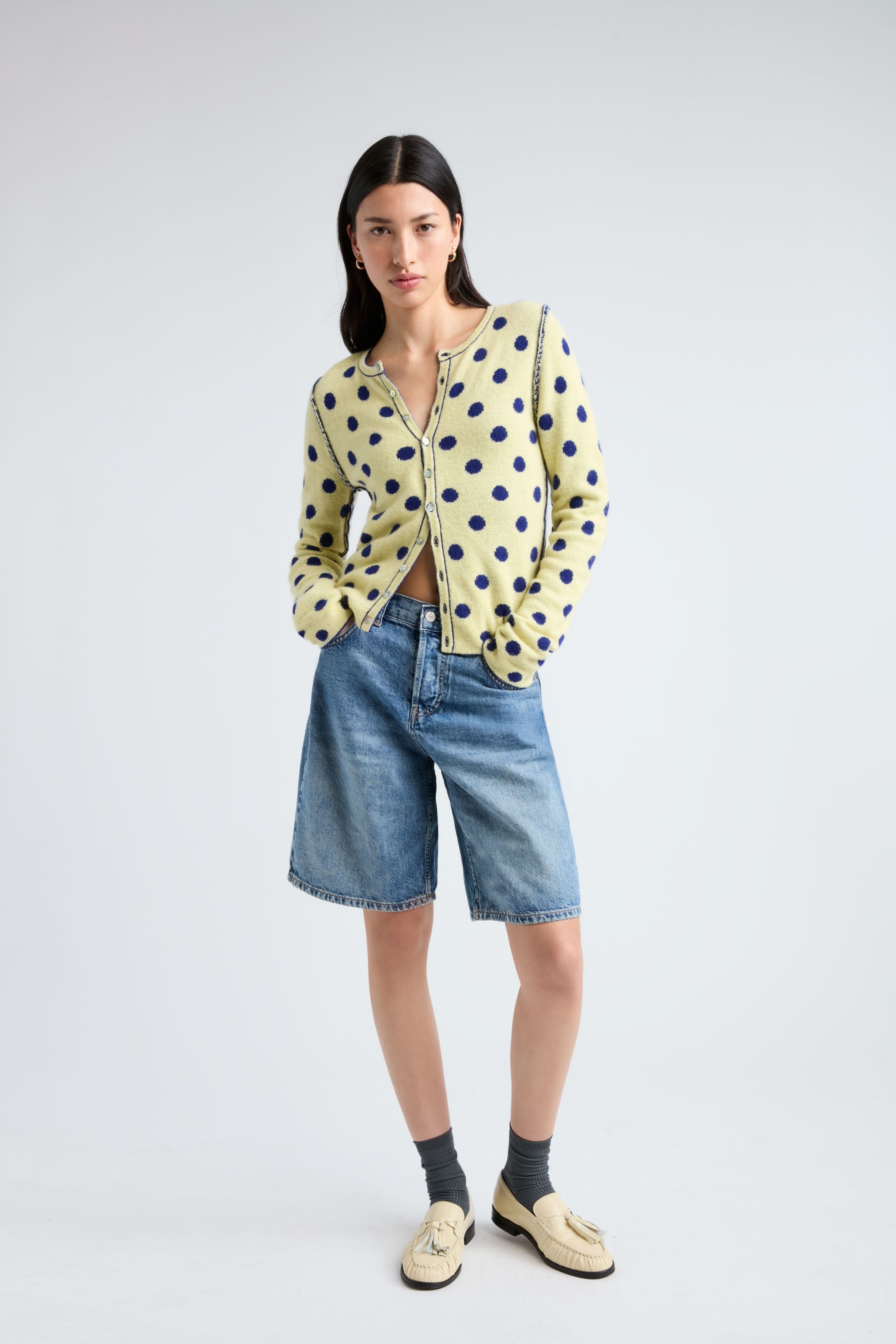 woman in denim shorts wearing a polka dot cardigan.