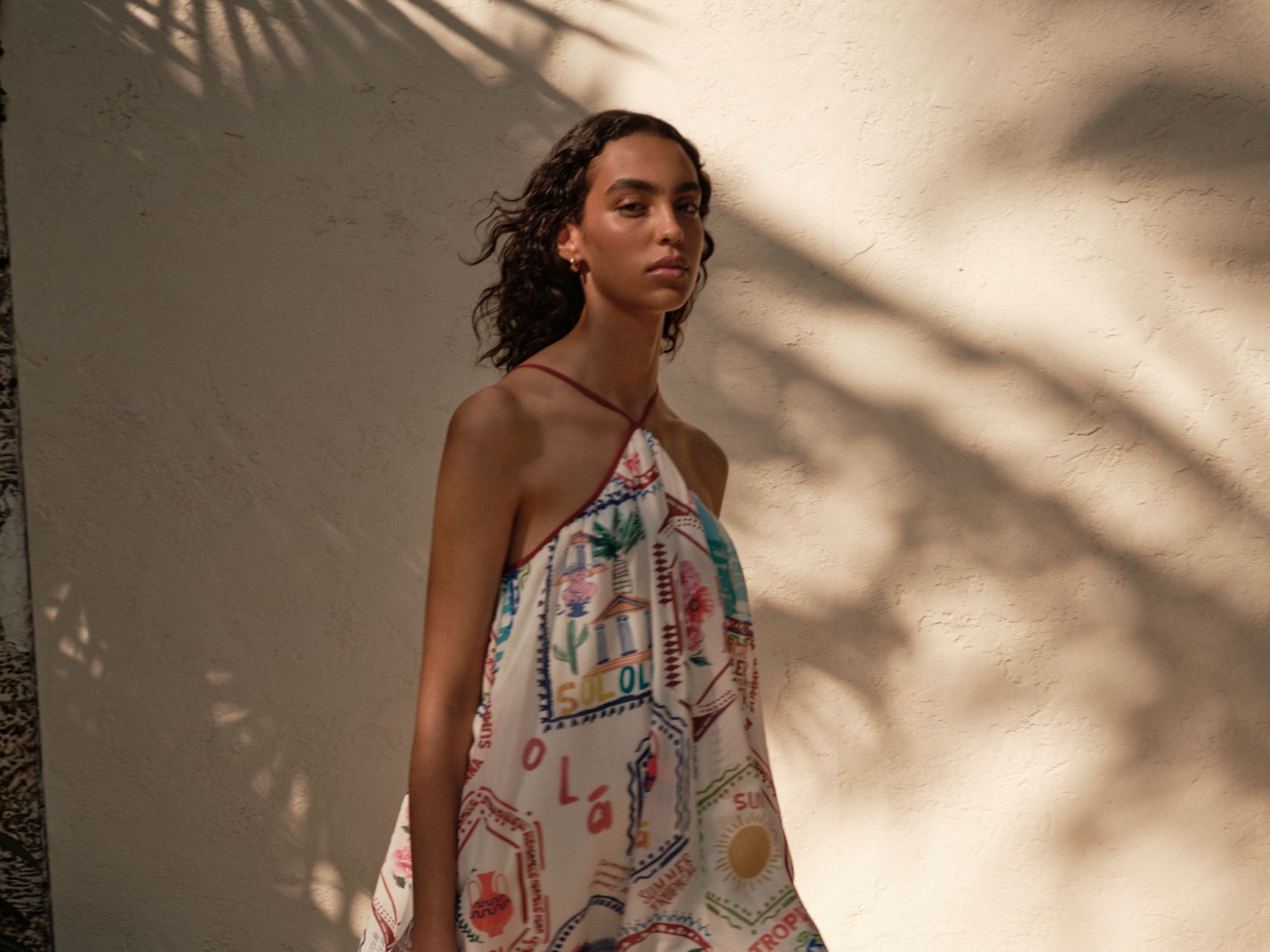 Woman wearing a printed mini dress and holding a woven tote bag.