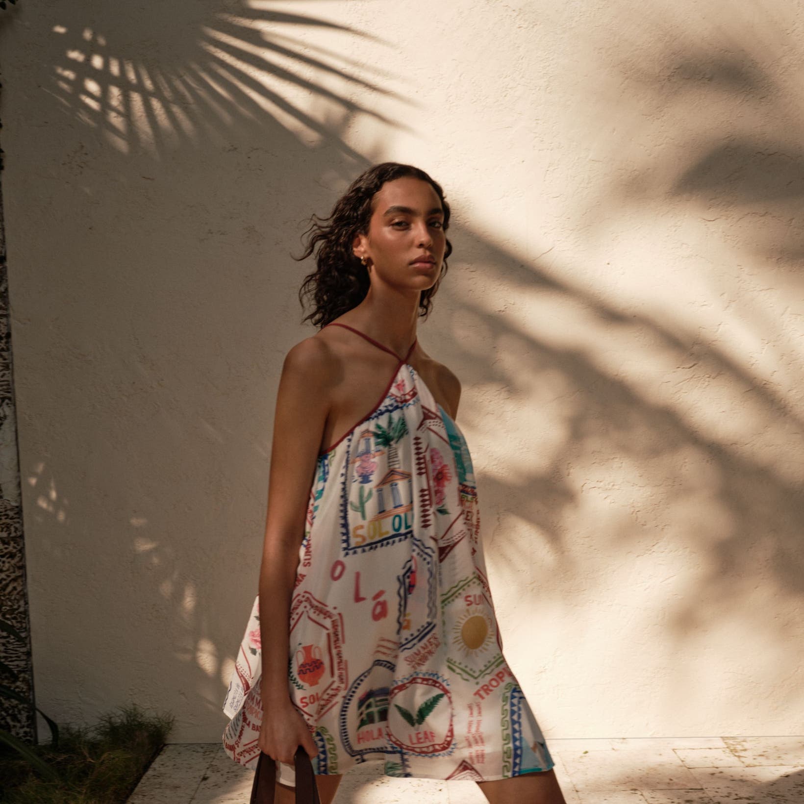 Woman wearing a printed mini dress and holding a woven tote bag.