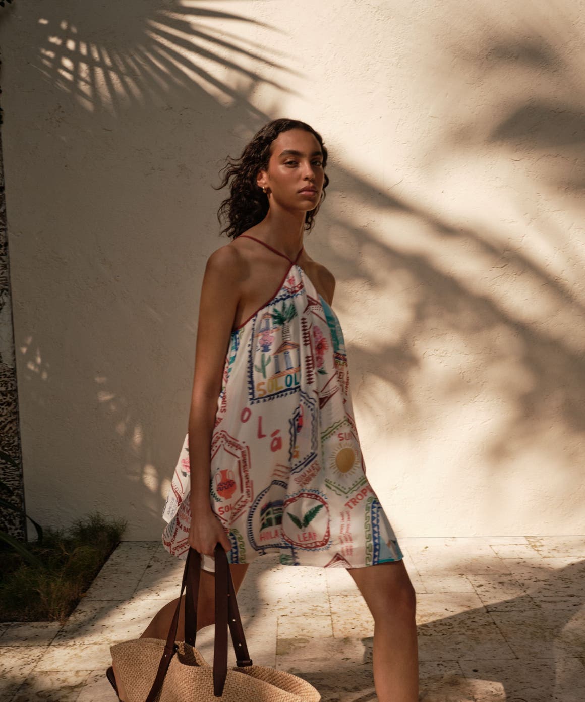Woman wearing a printed mini dress and holding a woven tote bag.