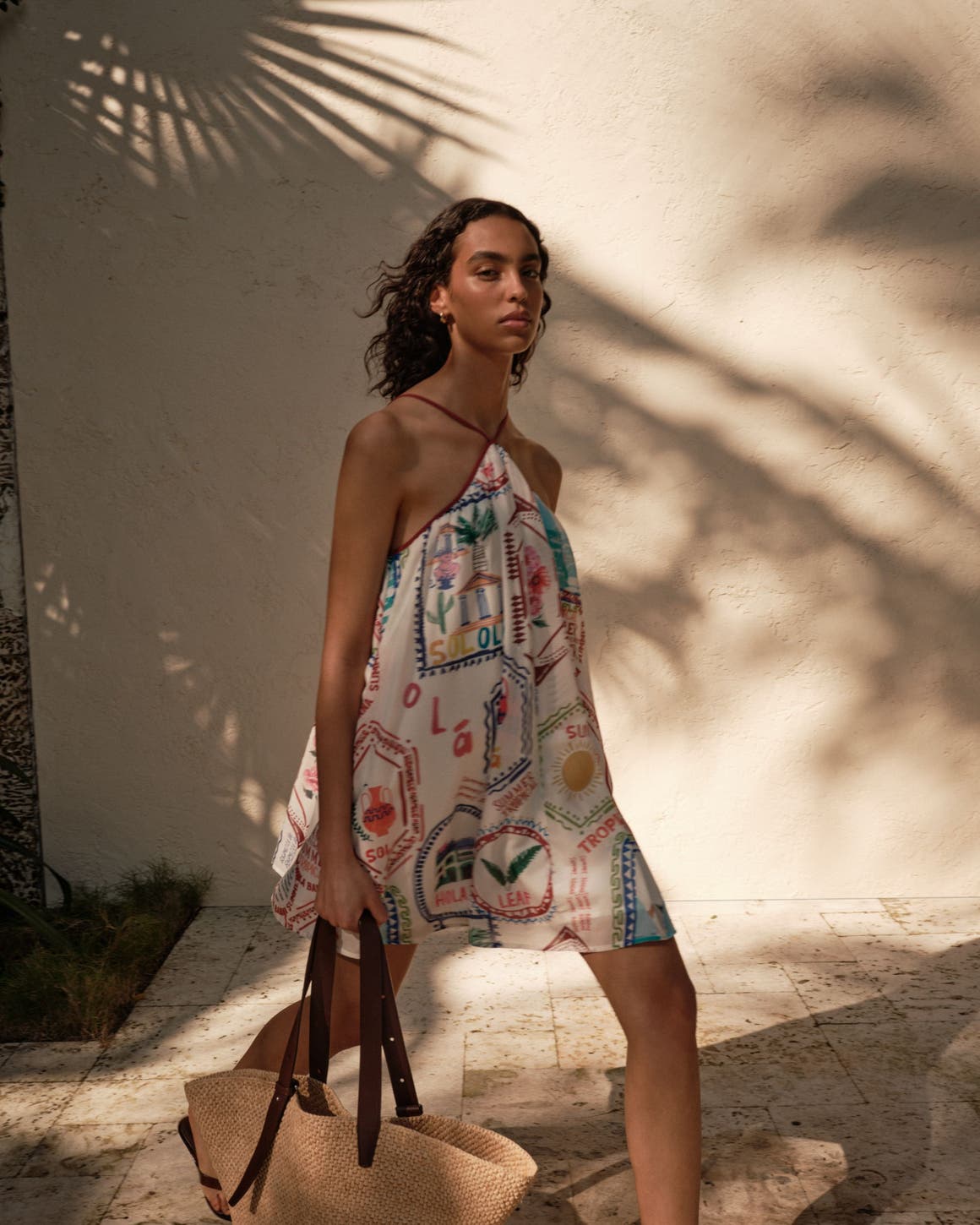 Woman wearing a printed mini dress and holding a woven tote bag.