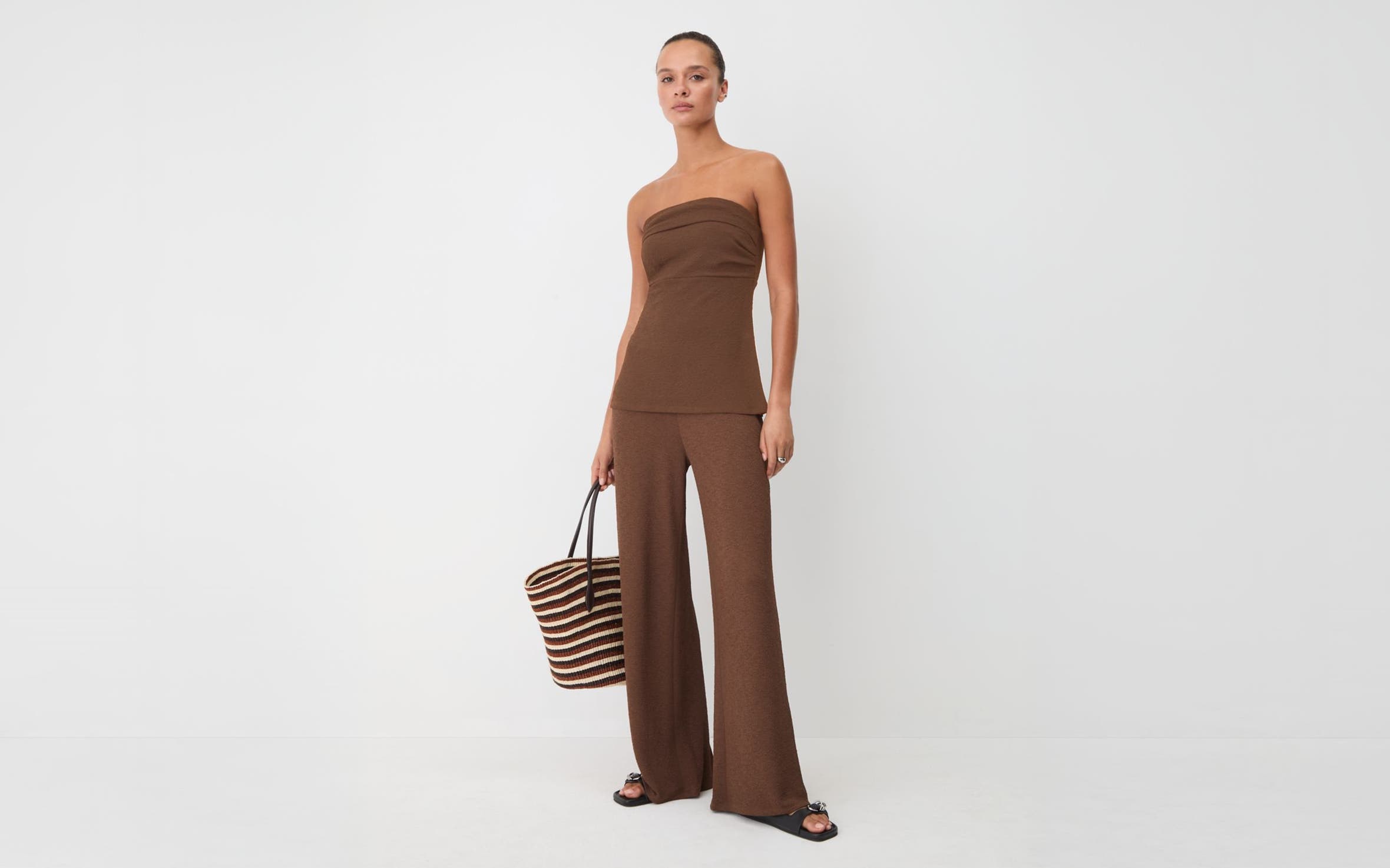 Woman wearing a matching brown set with a striped tote bag.