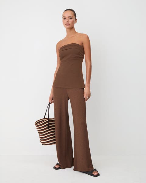 A woman wearing a strapless brown top with matching pants.