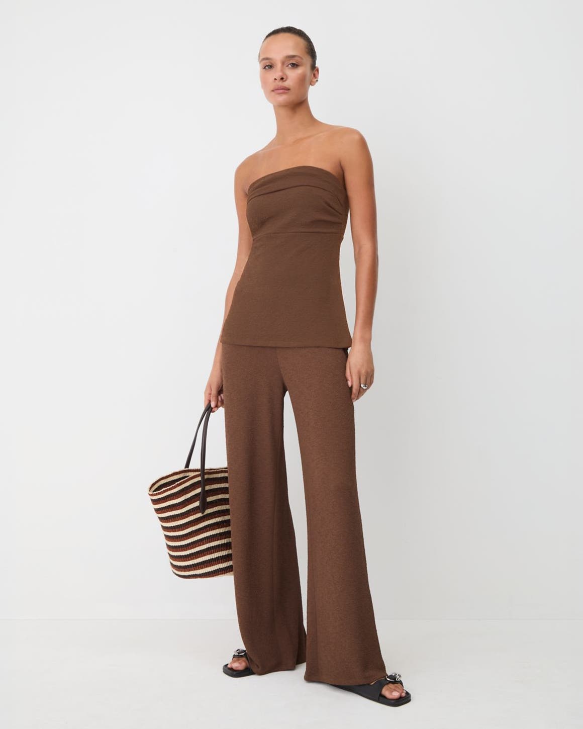 Woman wearing a matching brown set with a striped tote bag.