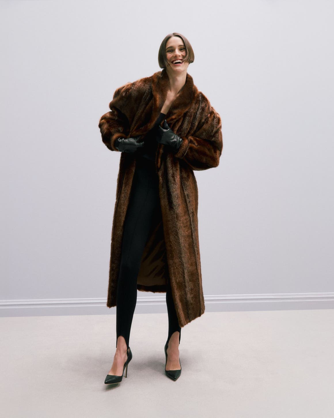 Woman wearing a faux fur coat, leggings, sunglasses and heels.