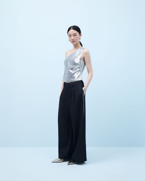 Woman wearing a sequined one-shoulder top and flowy pants.