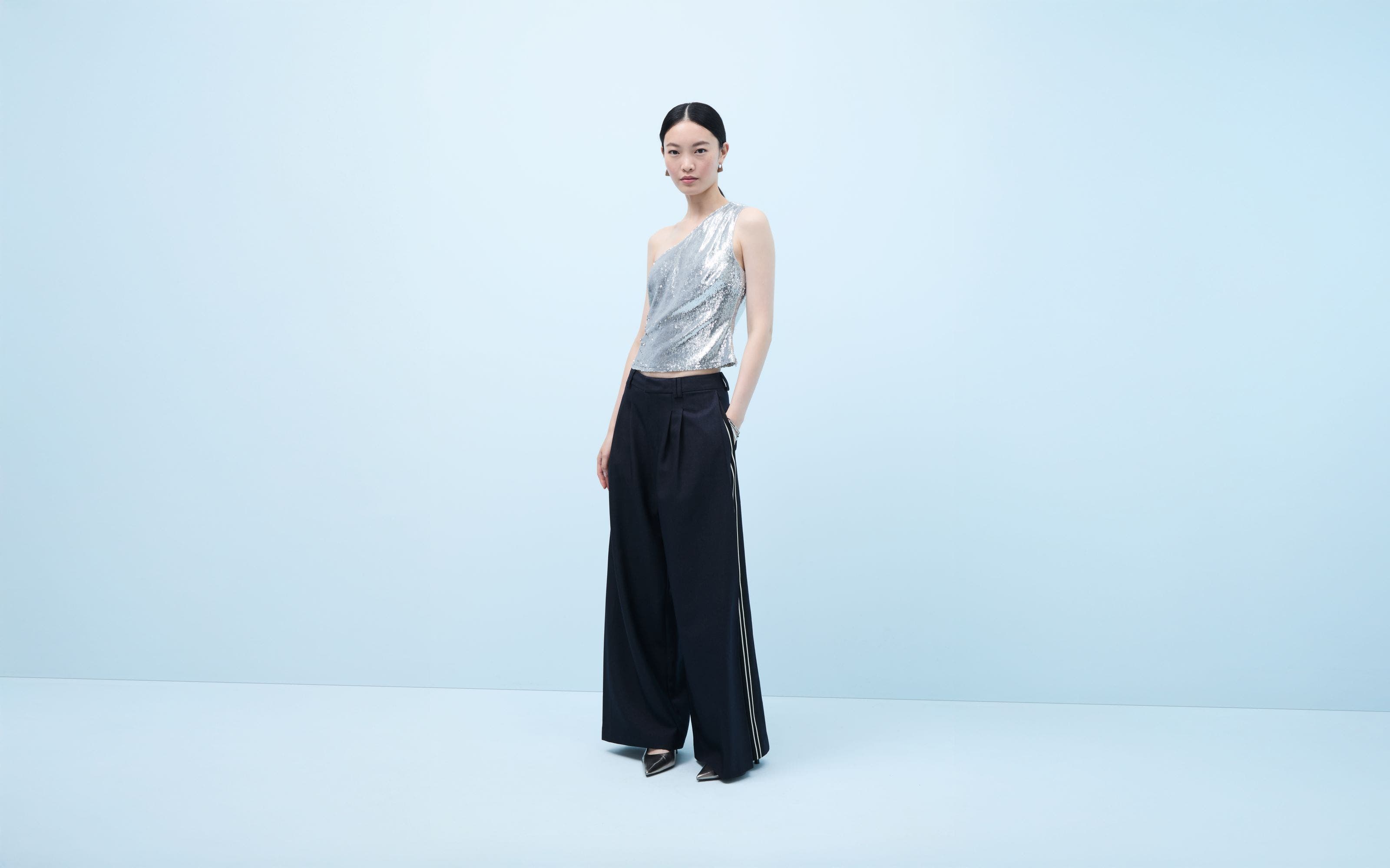 A woman wearing a sparkly silver one-shoulder top and trousers.