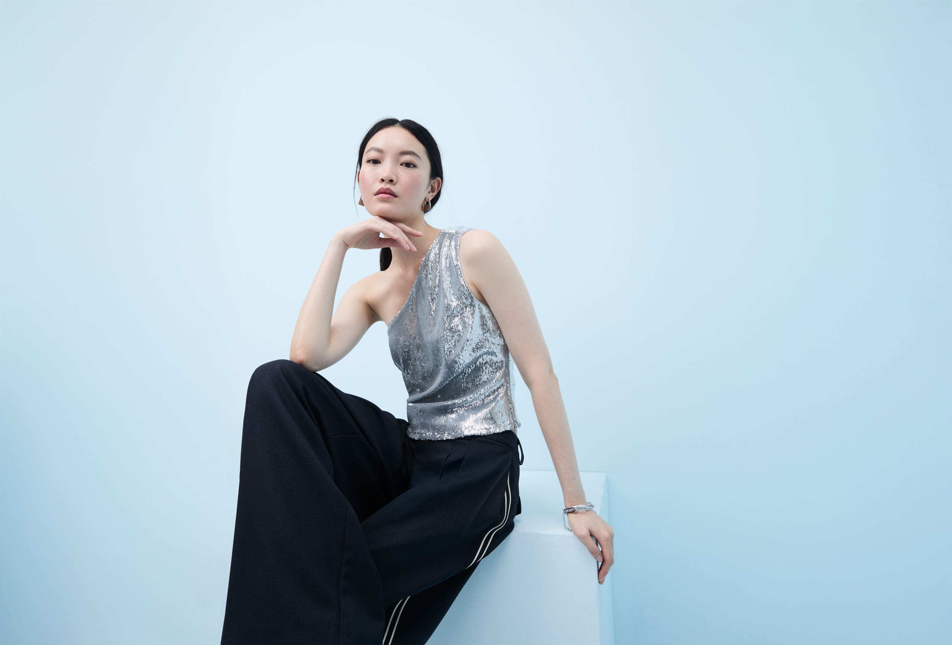 Woman wearing a sequined one-shoulder top and flowy pants.