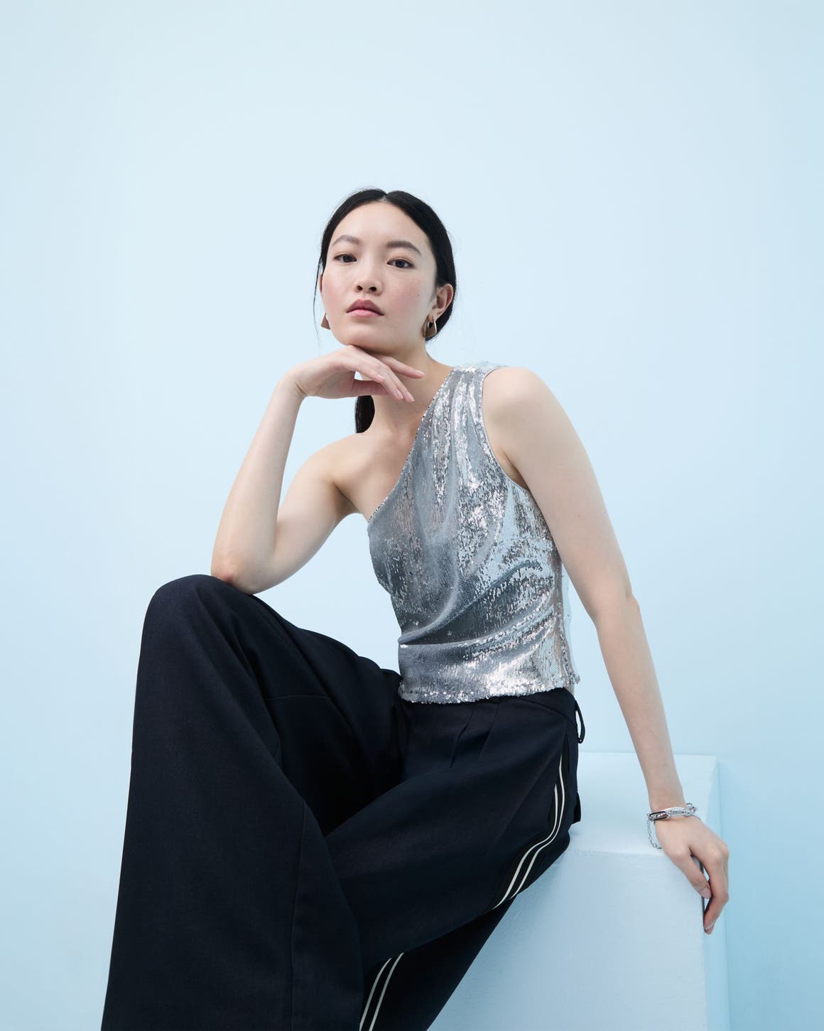 Woman wearing a sequined one-shoulder top and flowy pants.