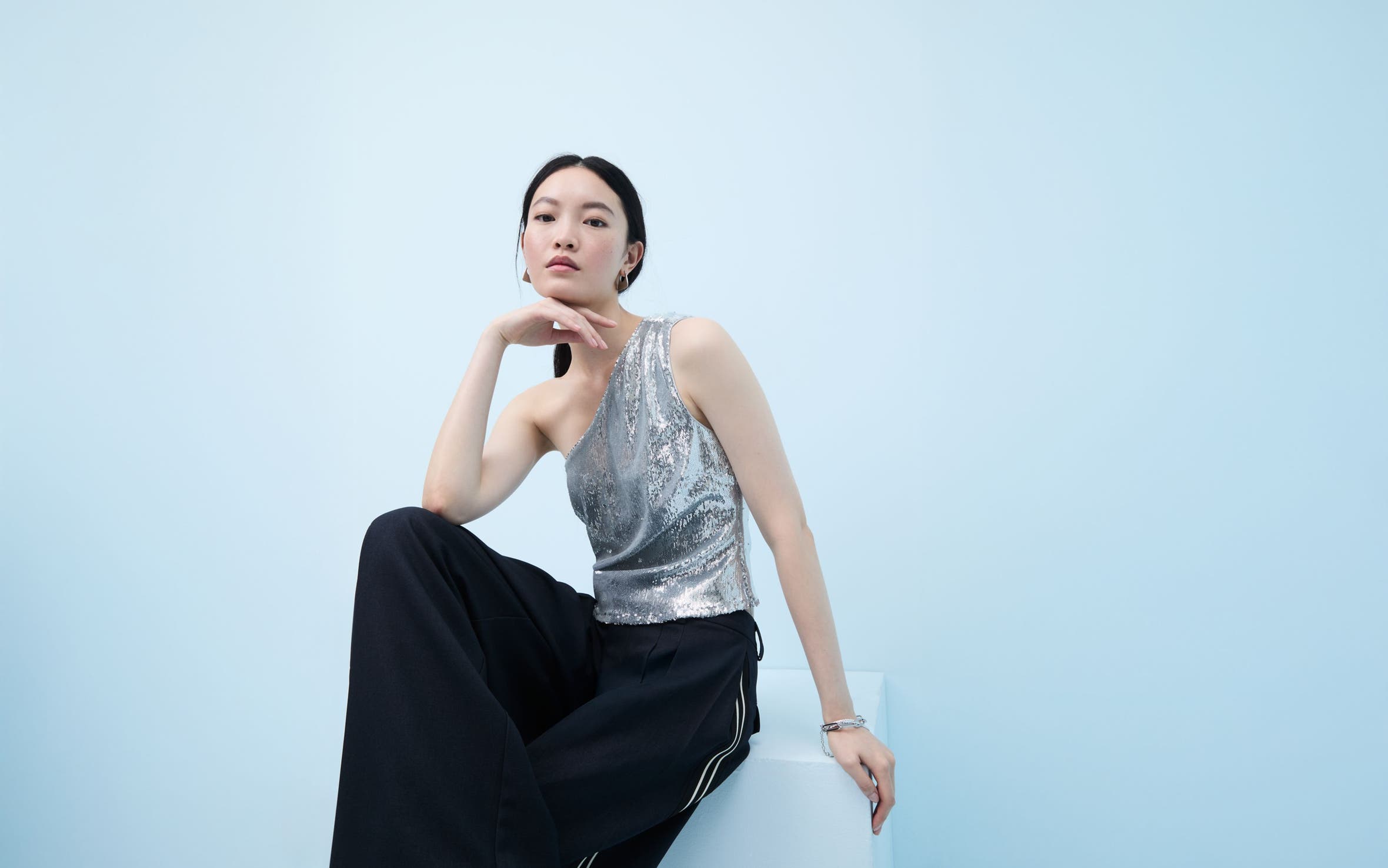 Woman wearing a sequined one-shoulder top and flowy pants.