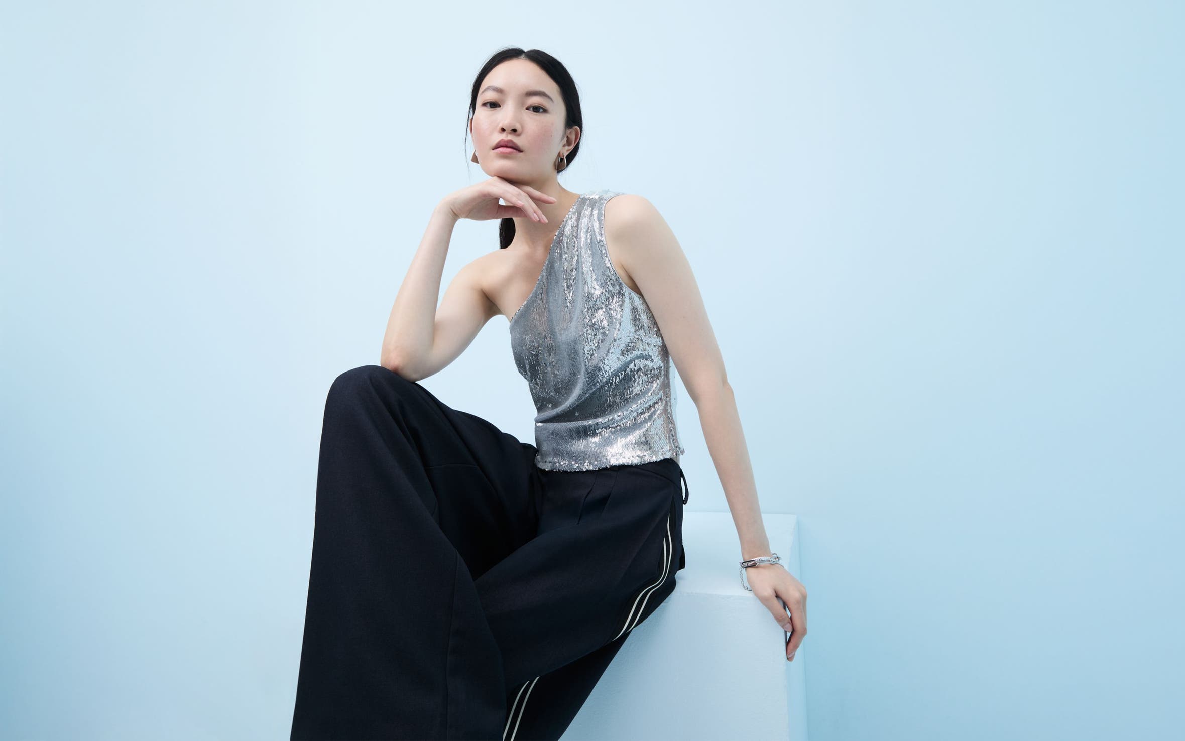 Woman wearing a sequined one-shoulder top and flowy pants.