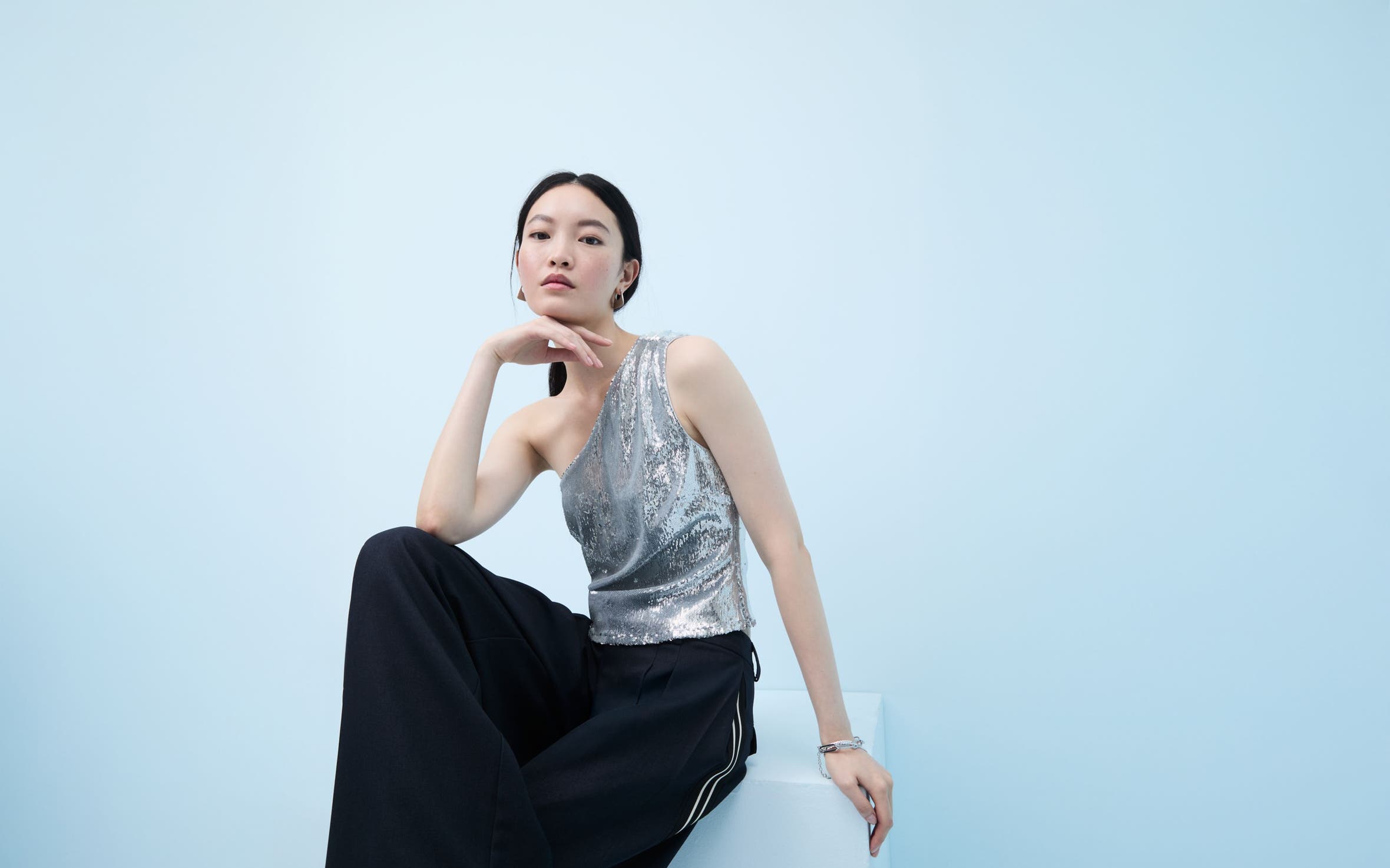 Woman wearing a sequined one-shoulder top and flowy pants.