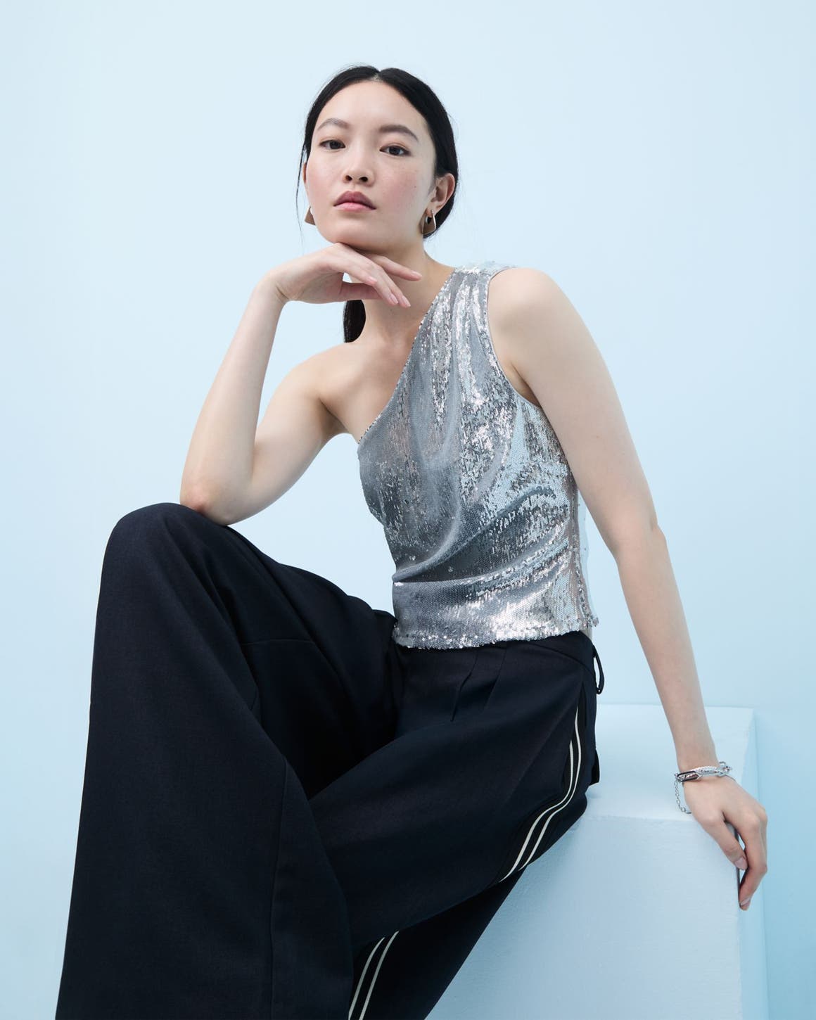 Woman wearing a sequined one-shoulder top and flowy pants.