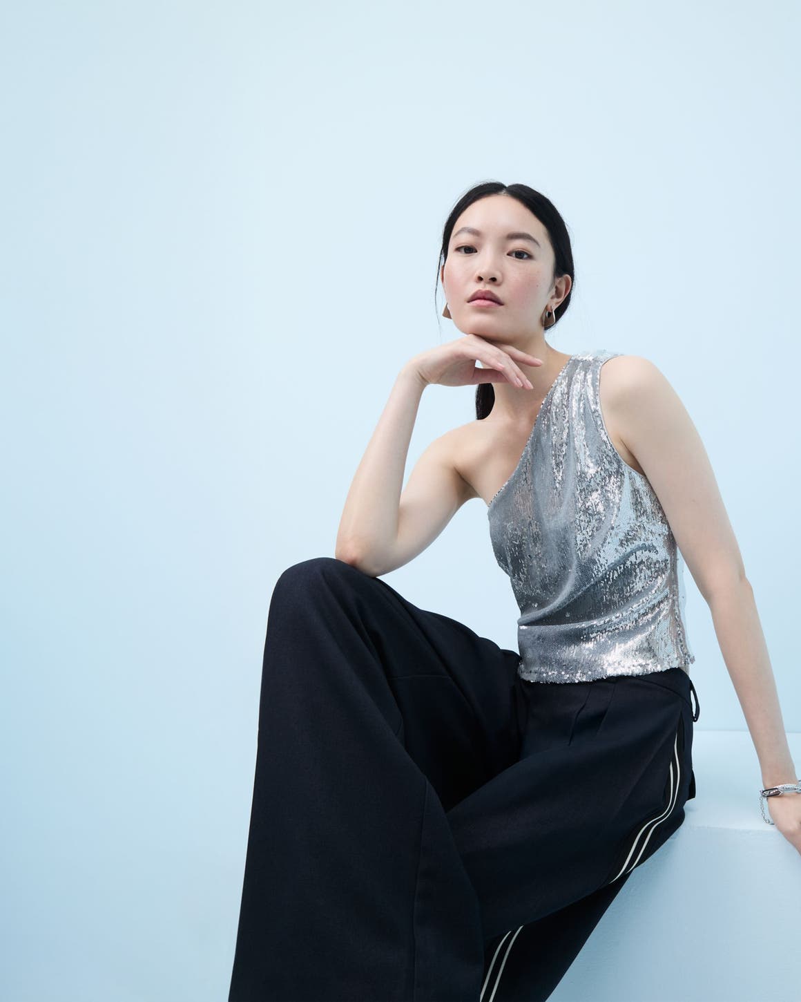 Woman wearing a sequined one-shoulder top and flowy pants.