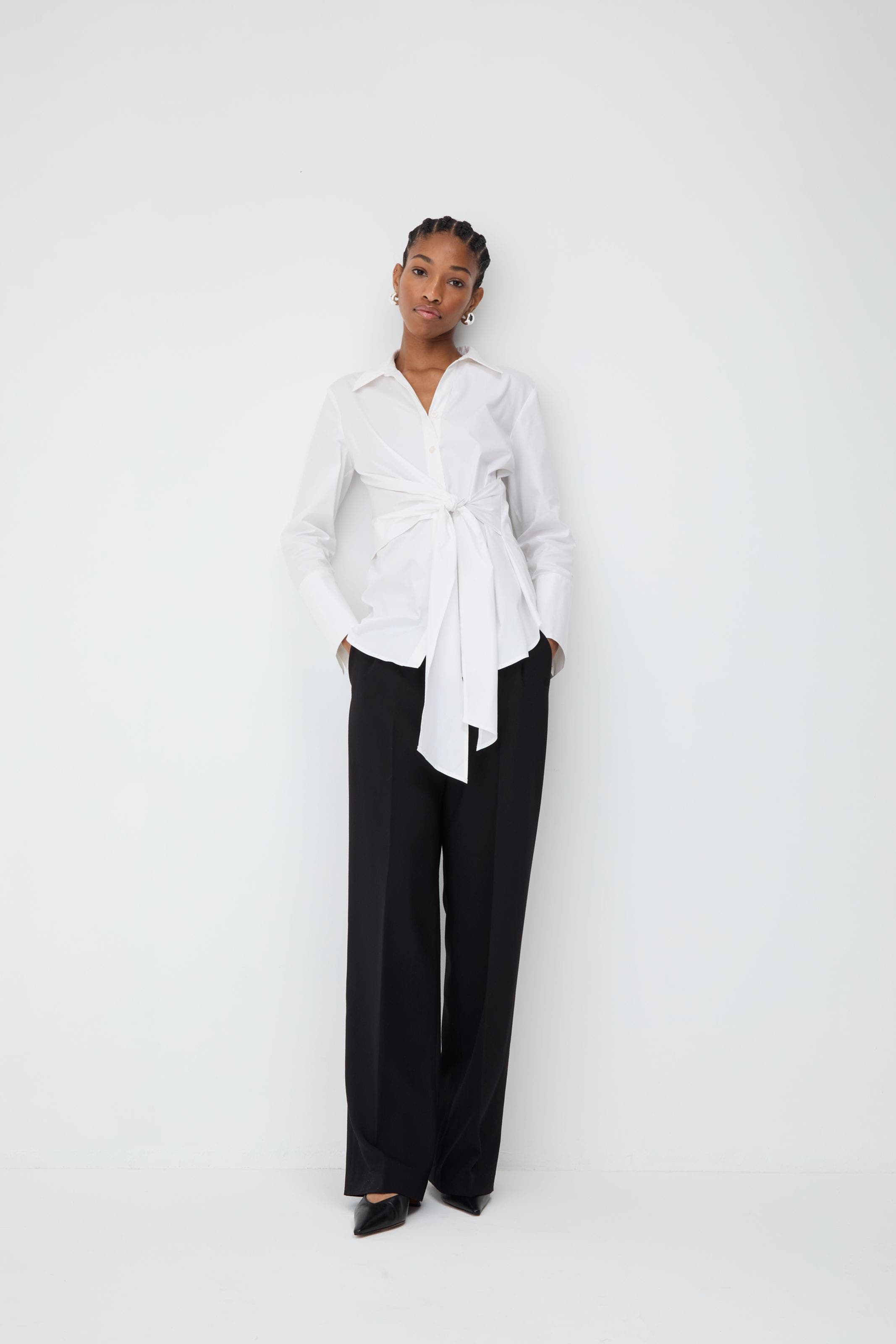 Woman wearing a white tie-front blouse and black pants.