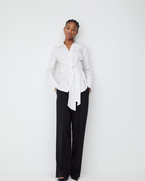 Woman wearing a white tie-front blouse and black pants.